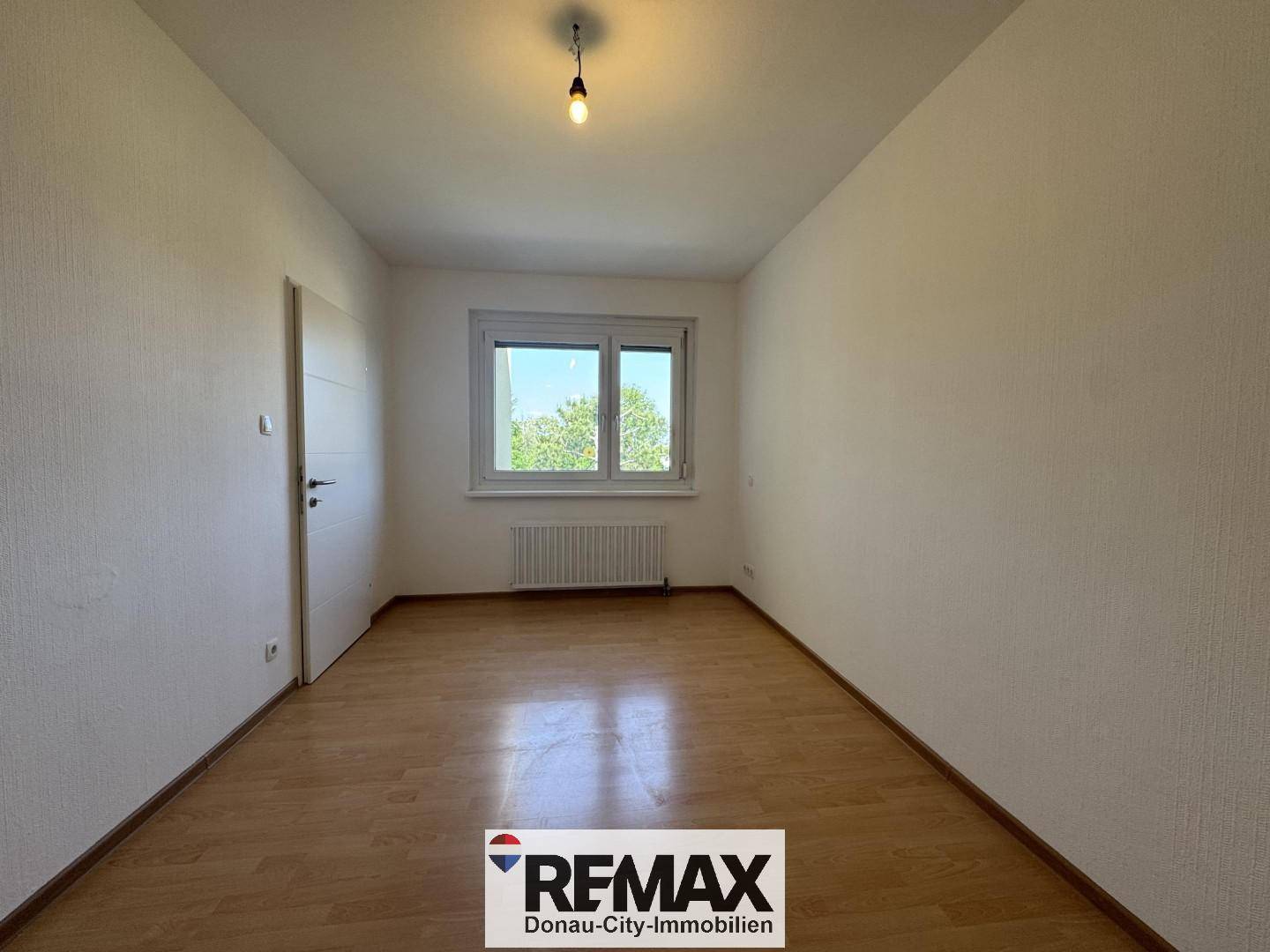 Leeres Schlafzimmer mit Laminatboden und einem Fenster, das viel Tageslicht hereinlässt.