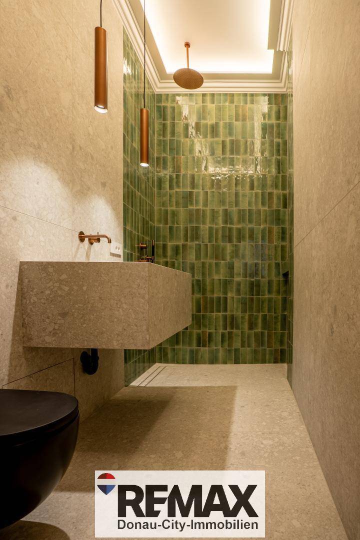 Elegantes Badezimmer mit schwarzer Wandtoilette, modernem Waschbecken und grüner Duschwand.