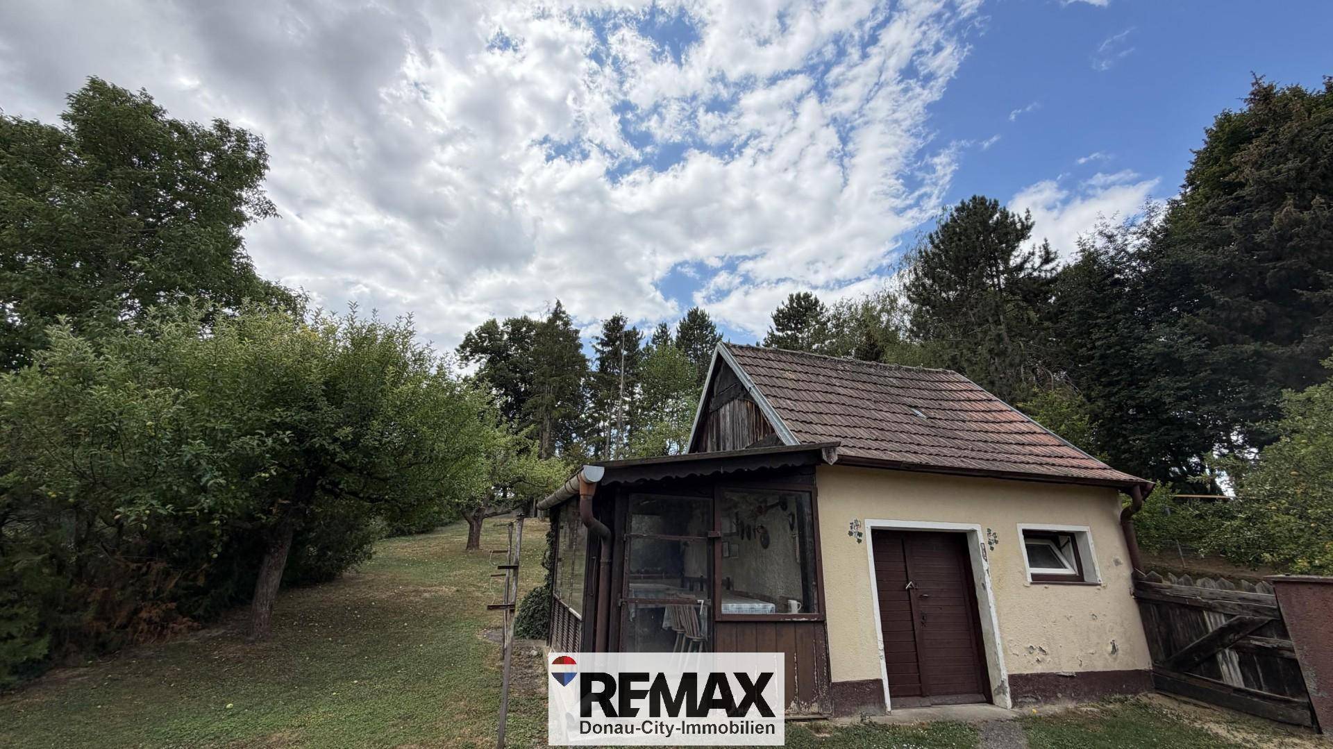 Kleines Nebengebäude im Grünen mit schrägem Dach und einfacher Holzveranda.