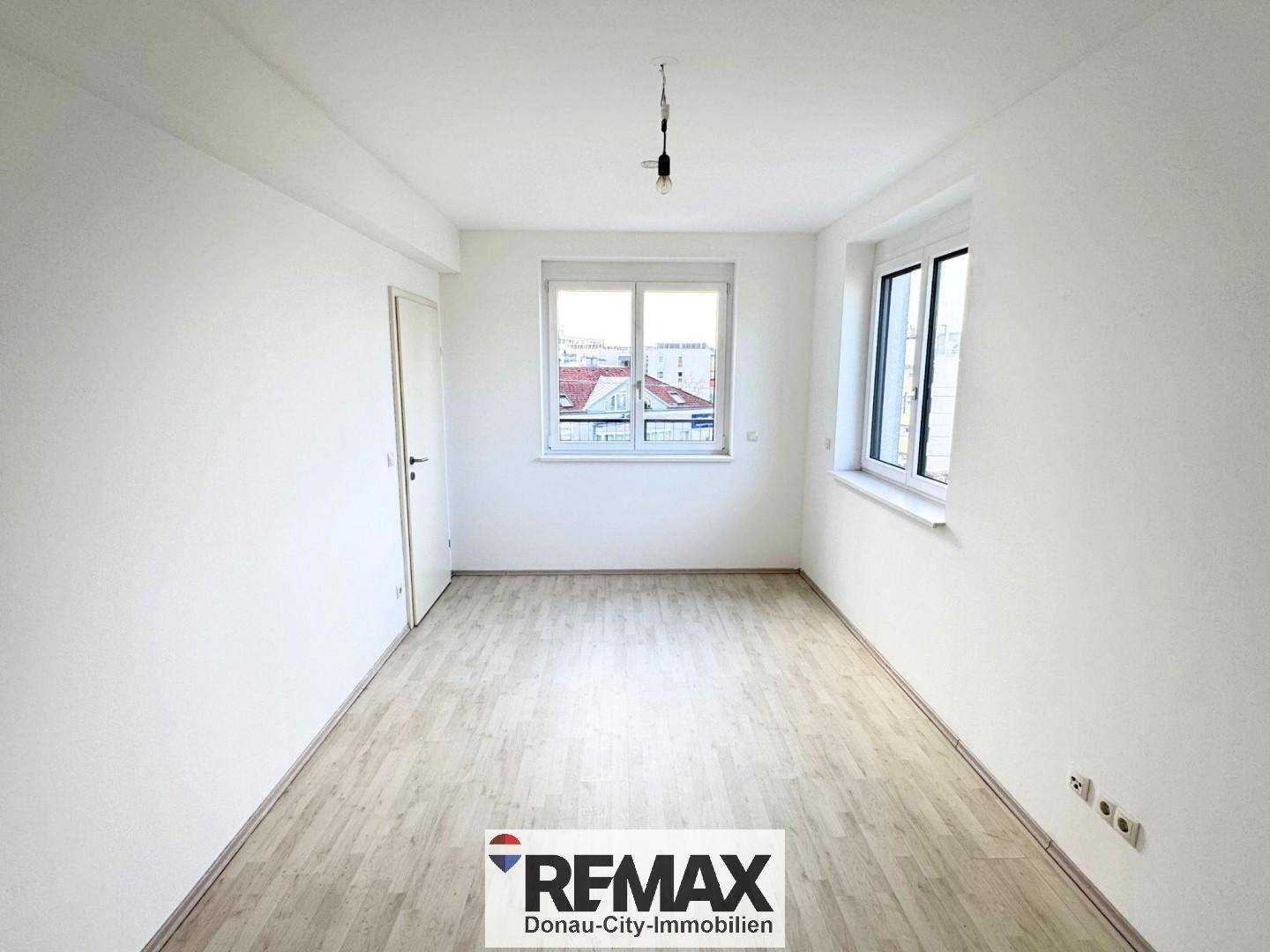 Freundliches Zimmer mit zwei Fenstern, hellen Wänden und Laminatboden.