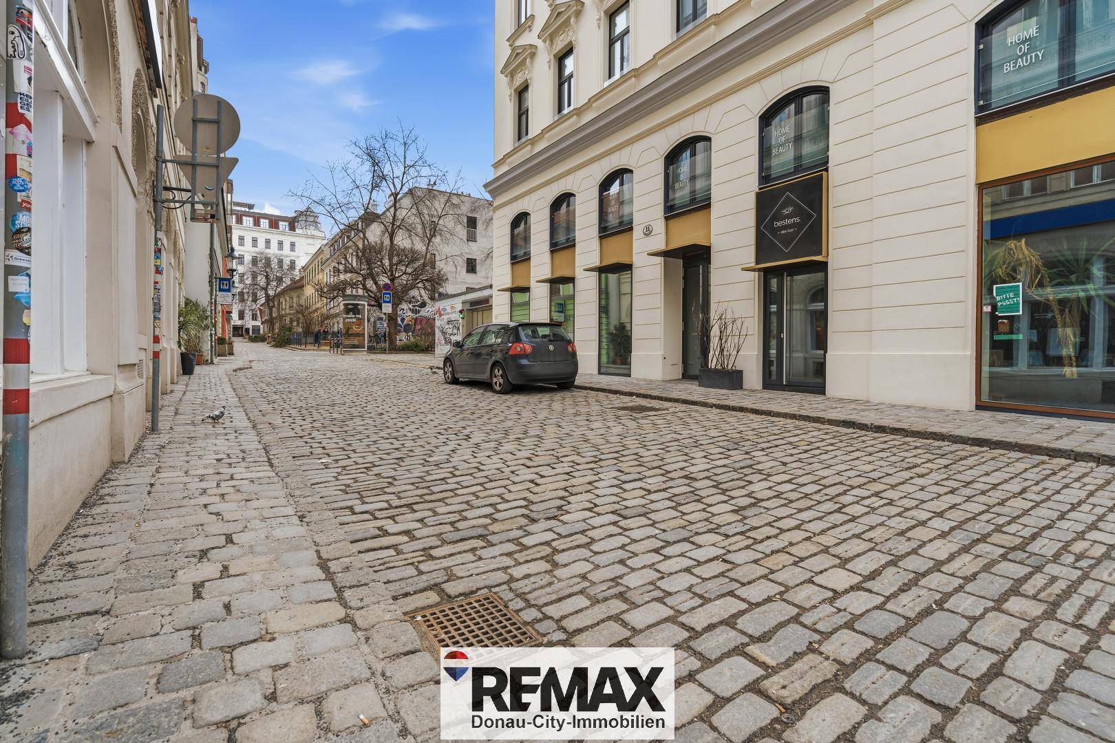 Kopfsteinpflasterstraße mit historischer Gebäudefassade und geparktem Auto in urbaner Umgebung.