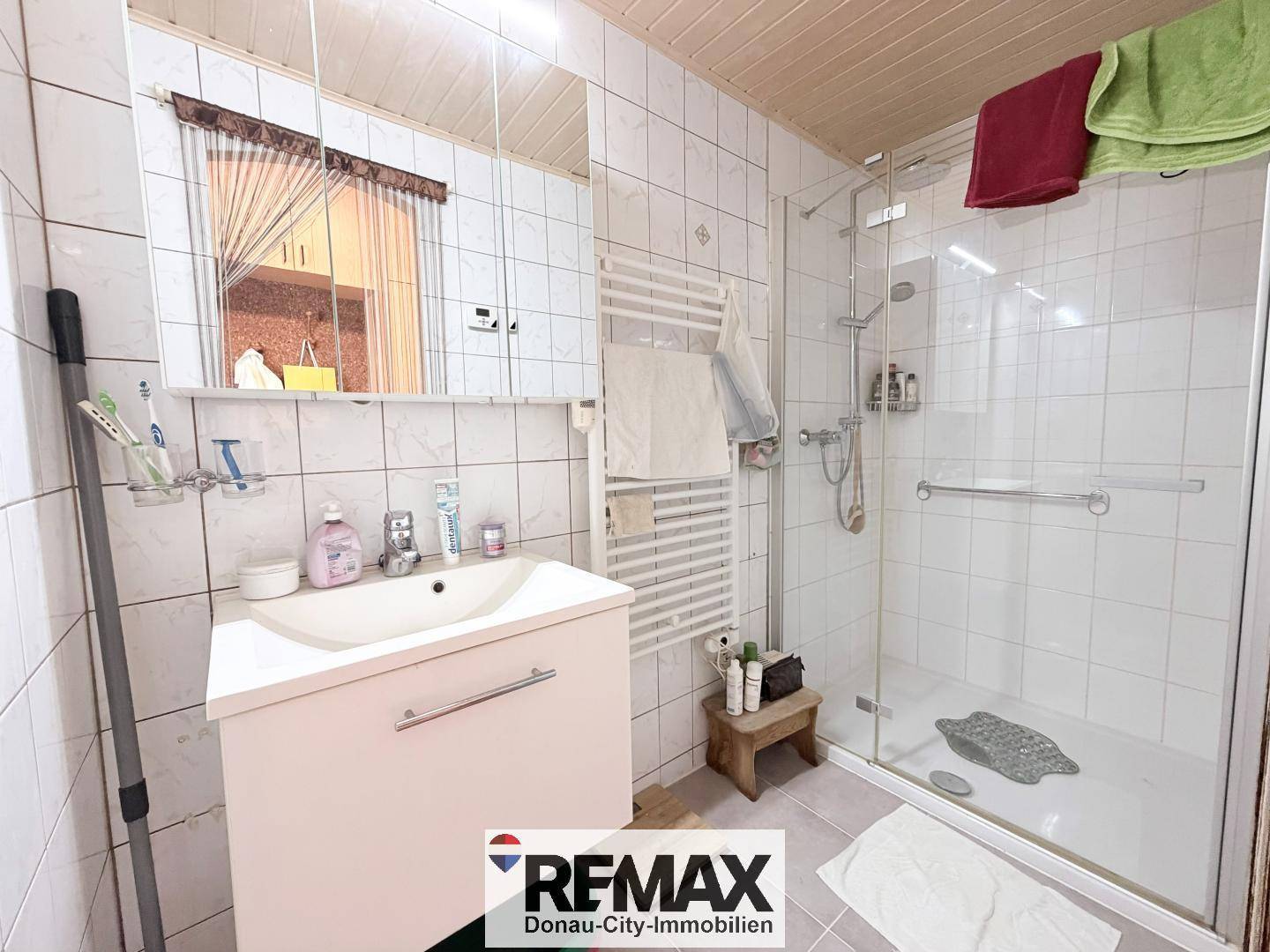 Helles Badezimmer mit Duschkabine, weißen Fliesen und beheiztem Handtuchhalter.