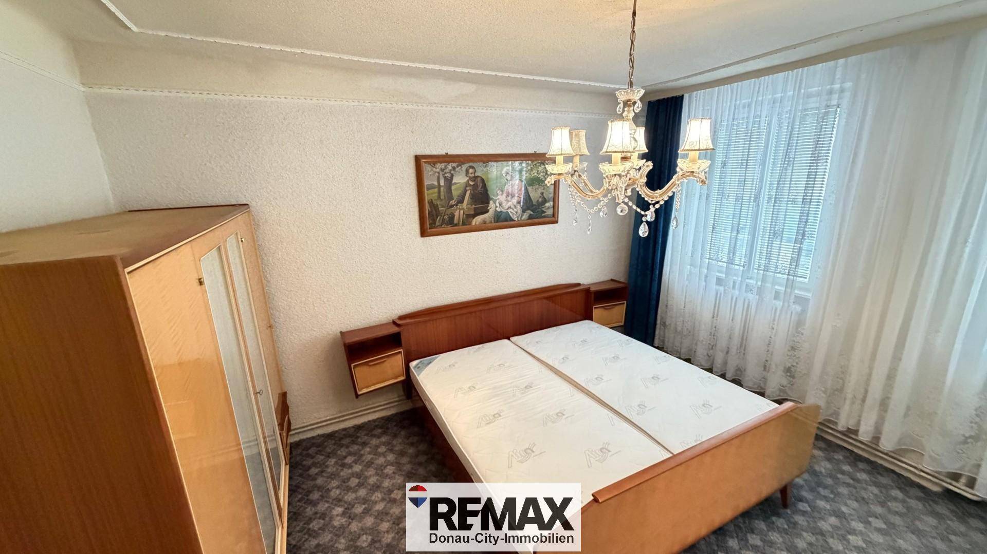 Schlafzimmer mit Doppelbett, Nachttischen und einem Kronleuchter, ausgestattet mit Teppichboden.