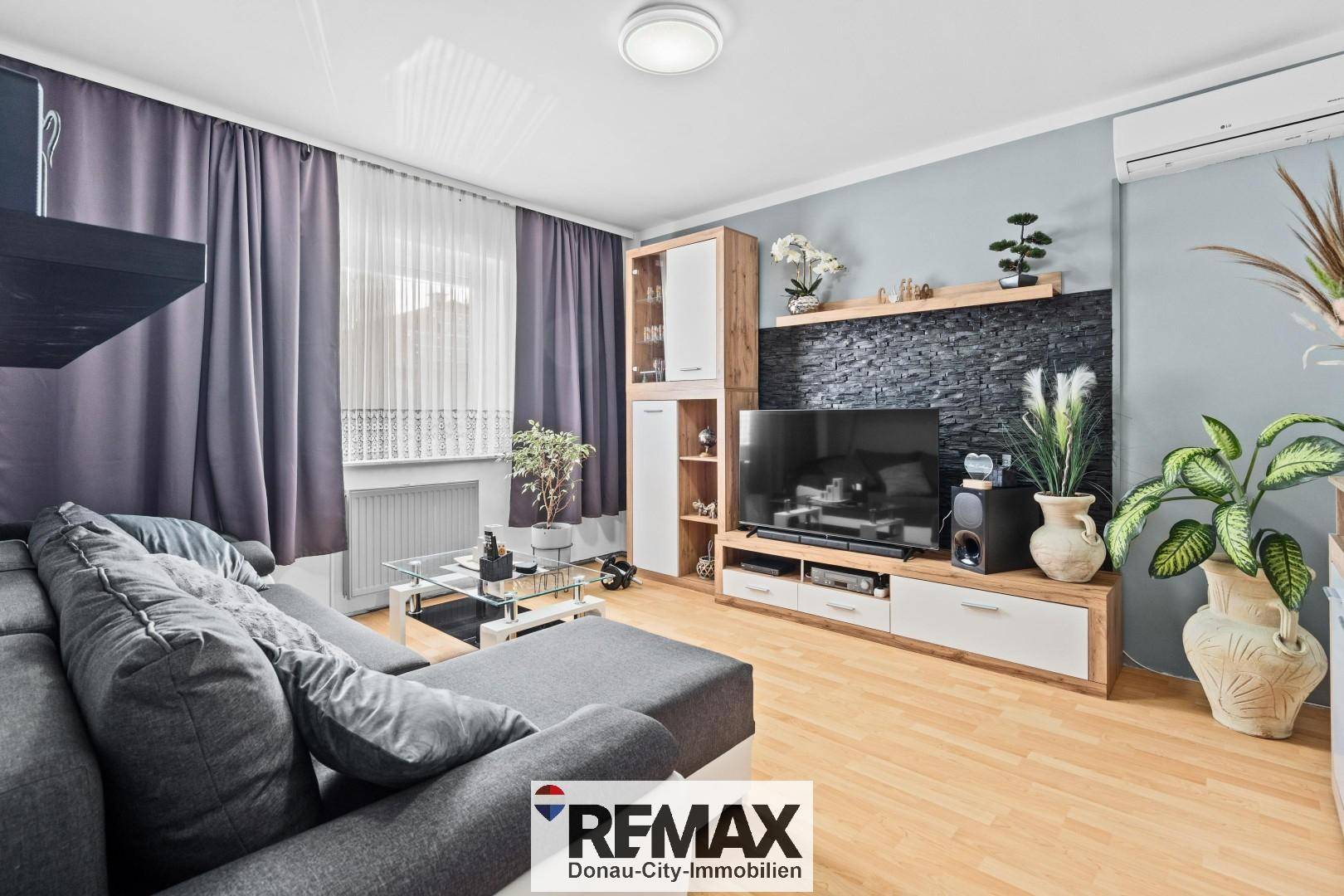 Gemütliches Wohnzimmer mit modernem Mediamöbel, Holzboden und Klimaanlage für angenehmes Raumklima.