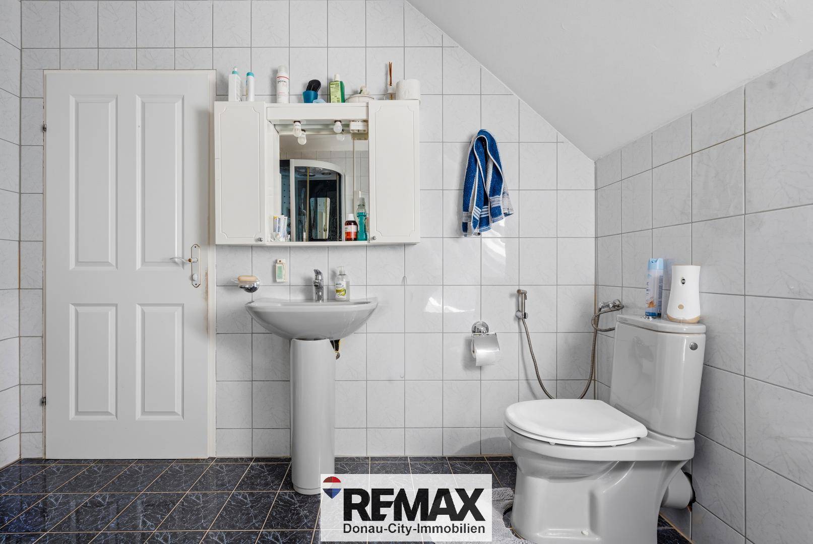 Gefliestes Gäste-WC mit Waschbecken, Toilette und Spiegelschrank unter Dachschräge.