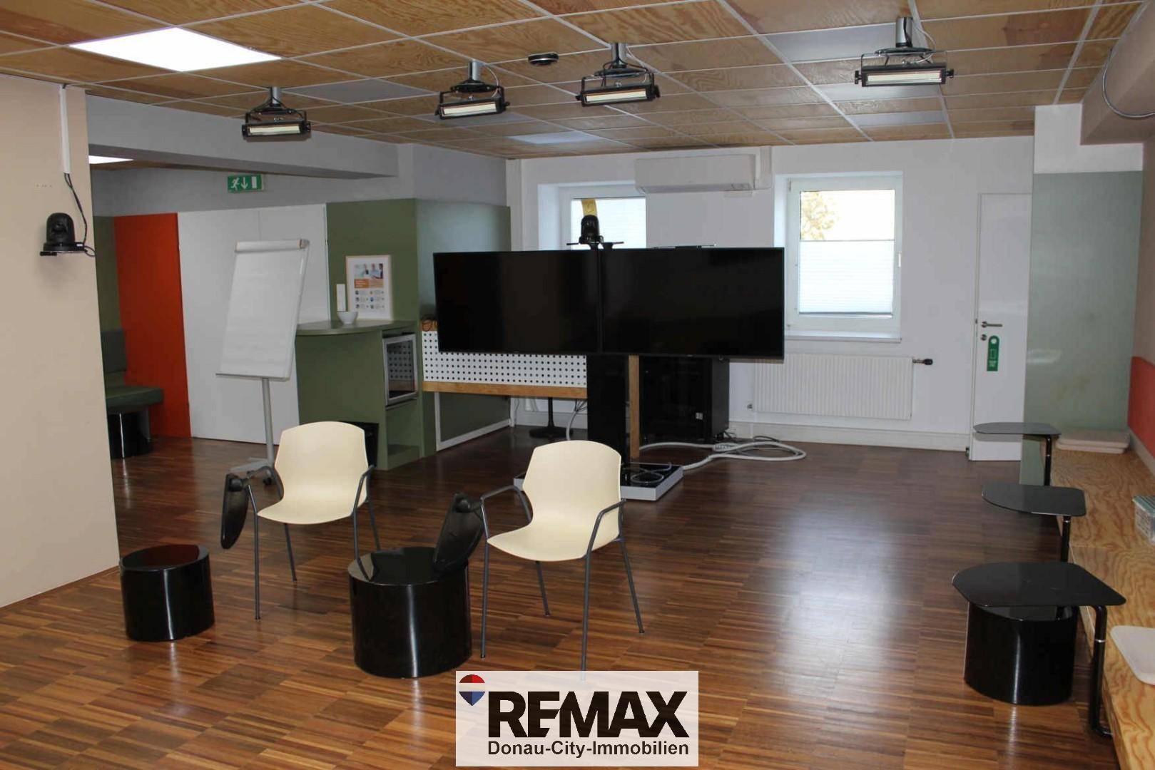 Moderner Präsentationsraum mit großer Leinwand, flexiblen Sitzgelegenheiten und Holzdeckenplatten.