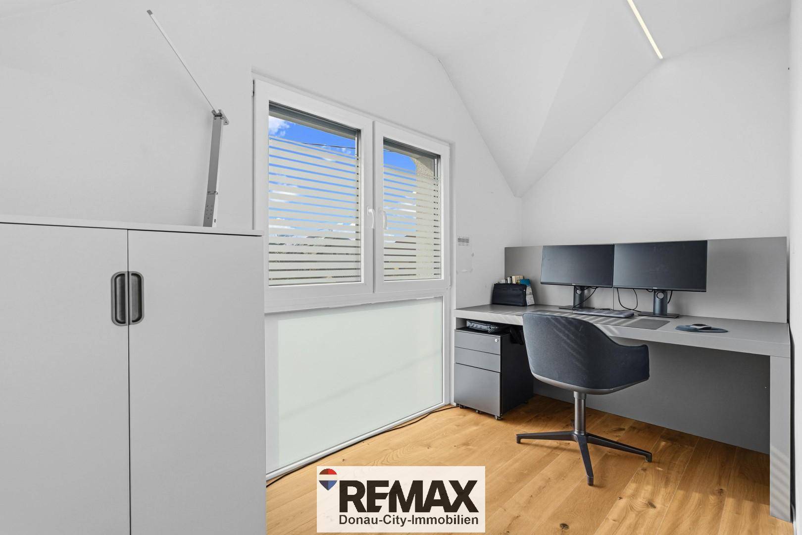 Helles Arbeitszimmer mit Schreibtisch, zwei Monitoren und Fenster unter der Dachschräge.
