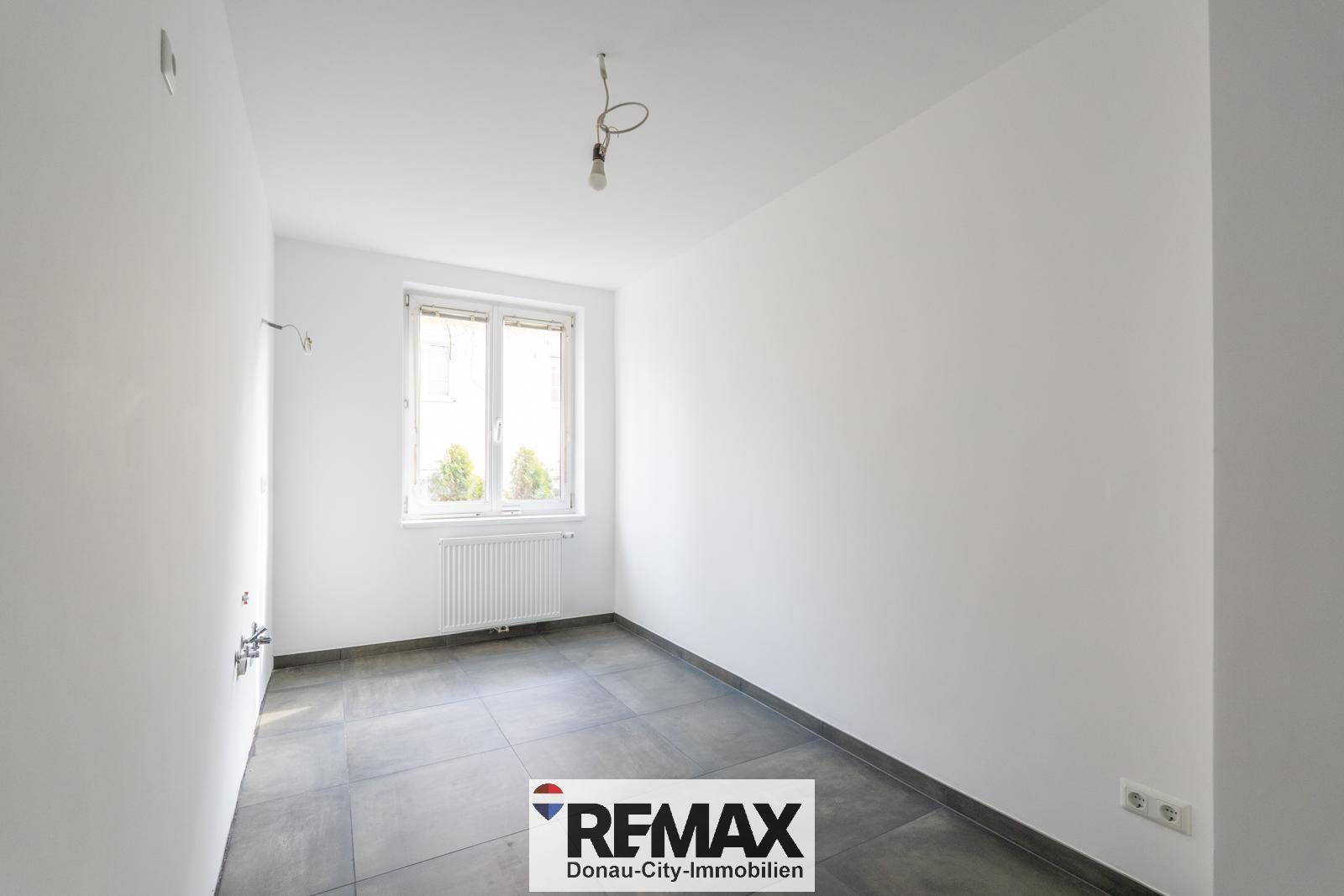 Leerer Raum mit dunklen Fliesen, weißen Wänden und Fenster, ideal für eine Küche.