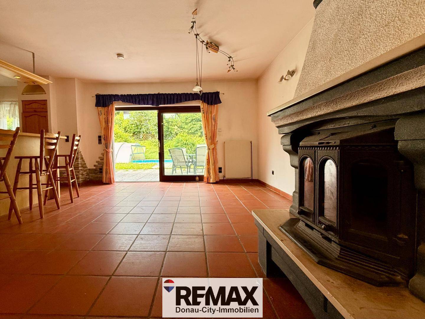 Geräumiges Wohnzimmer mit traditionellem Kaminofen, Terracottaboden und Zugang zum Außenbereich mit Pool.