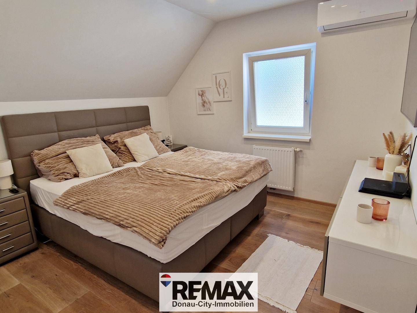 Gemütliches Schlafzimmer mit Doppelbett, Holzfußboden, Fenster und Klimaanlage.