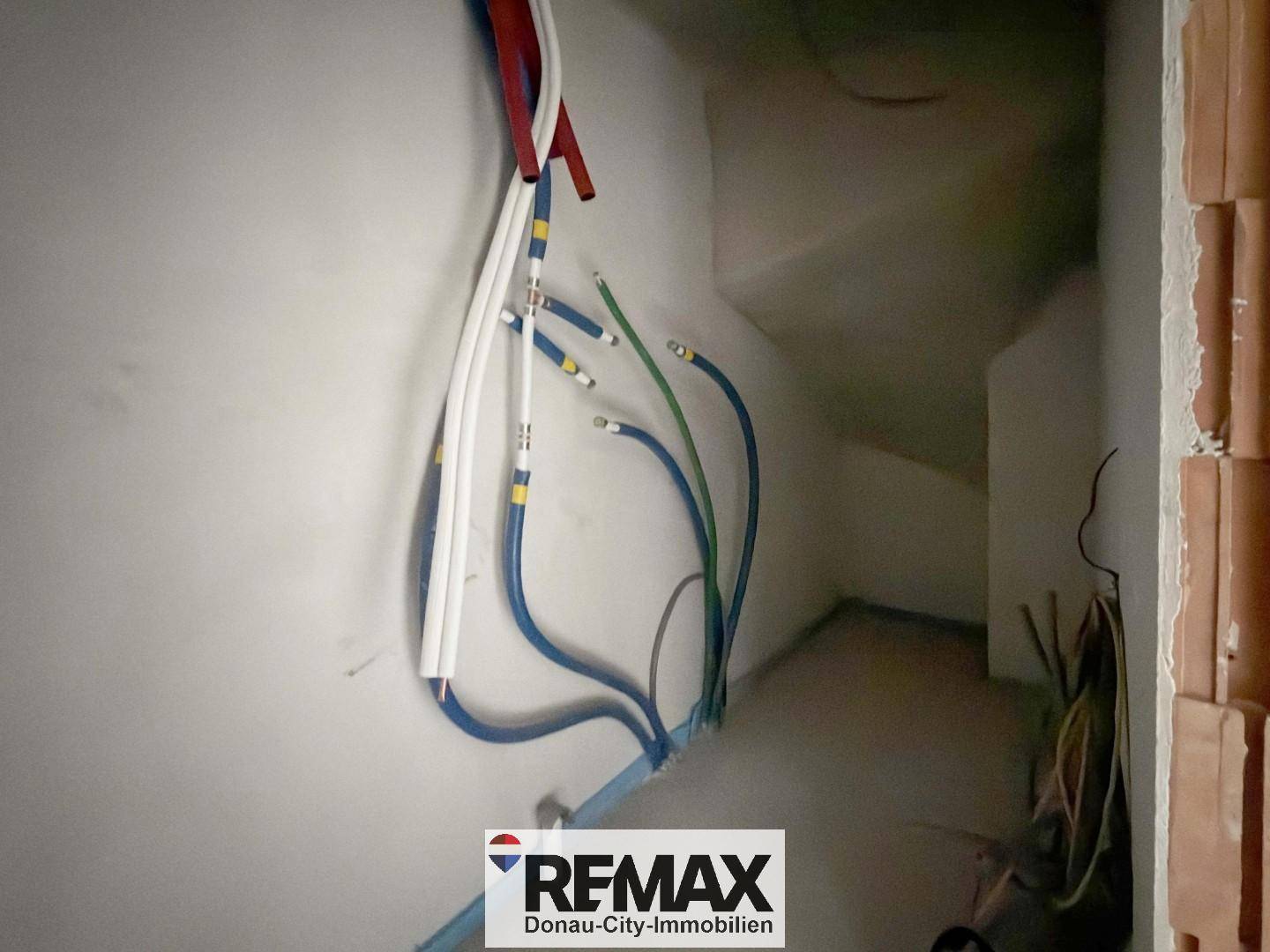 Innenraum im Rohbau mit sichtbaren Leitungen und Verkabelung an der Wand.