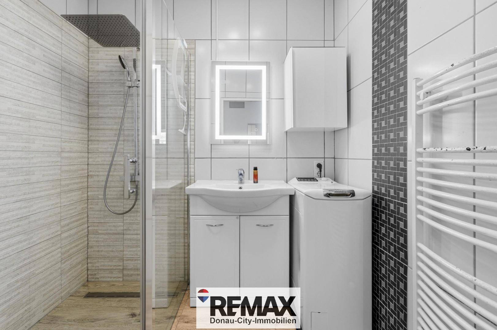 Modernes Badezimmer mit ebenerdiger Dusche, Waschbecken, beleuchtetem Spiegel und Waschmaschine.