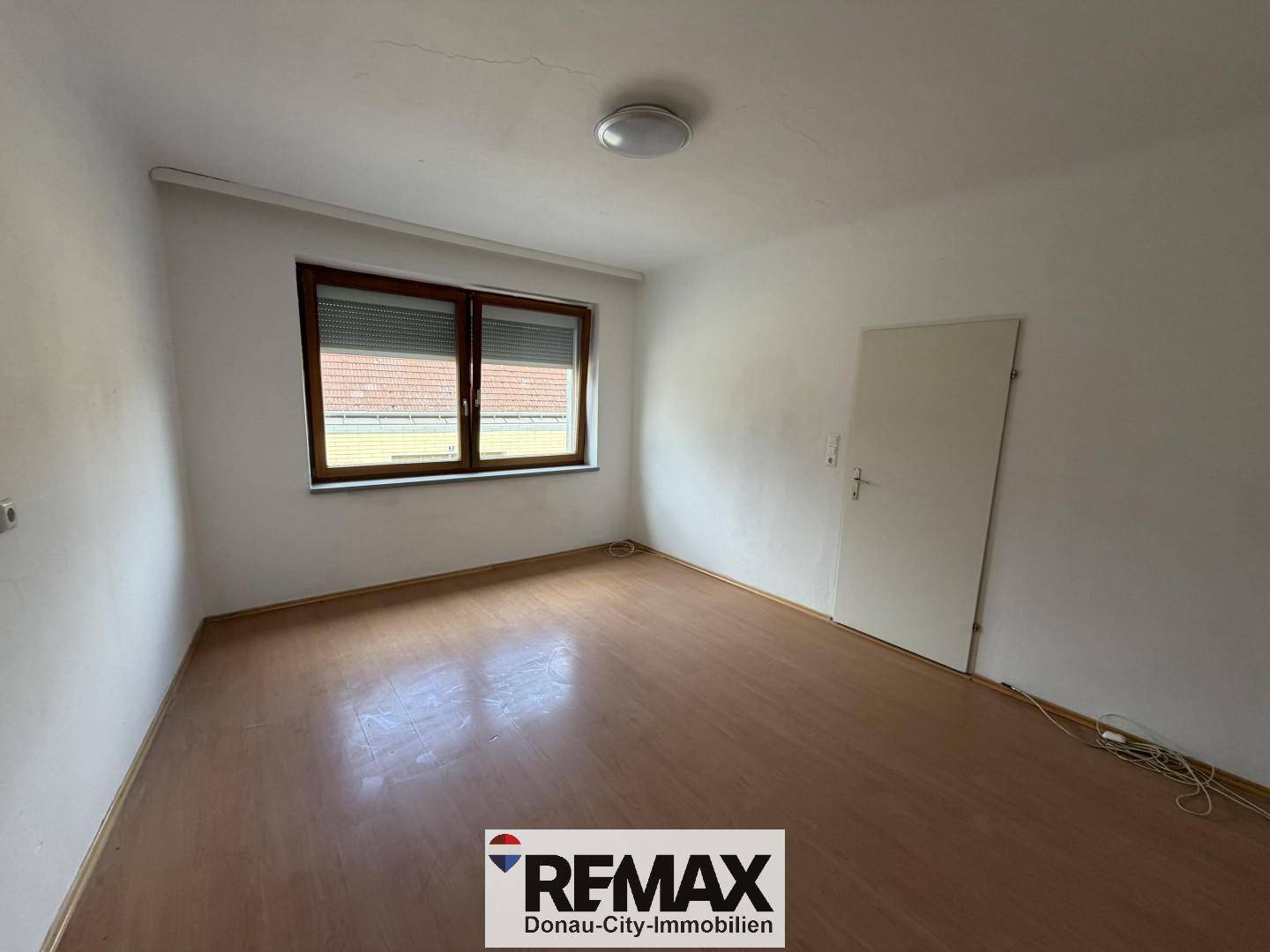 Leeres Zimmer mit Laminatboden und Fenster, vielseitig nutzbar als Wohn- oder Schlafzimmer.