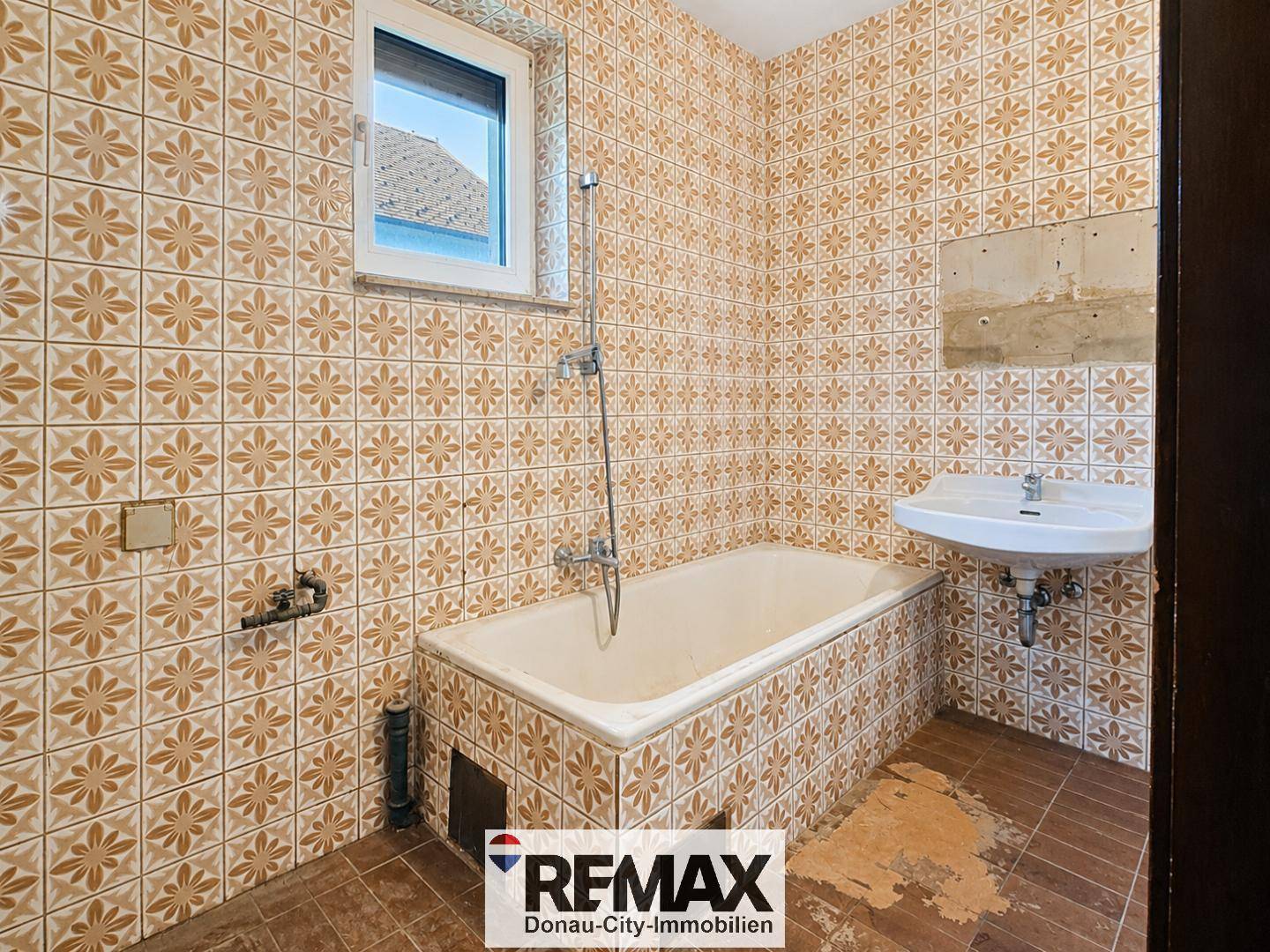 Badezimmer mit älteren Fliesen, Badewanne, Waschbecken und Fenster.