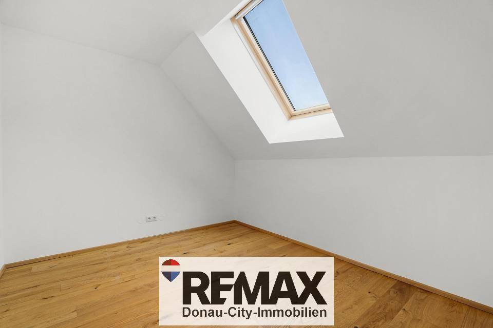 Leeres Zimmer mit Holzboden, weißen Wänden und einem schrägen Dachfenster für natürliches Licht.