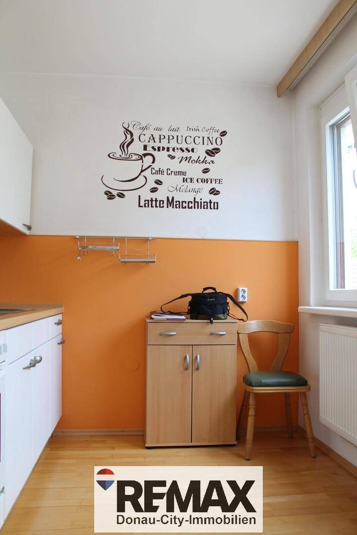 Küchenbereich mit Fenster, kleinem Schrank und dekorativer Wandbeschriftung.