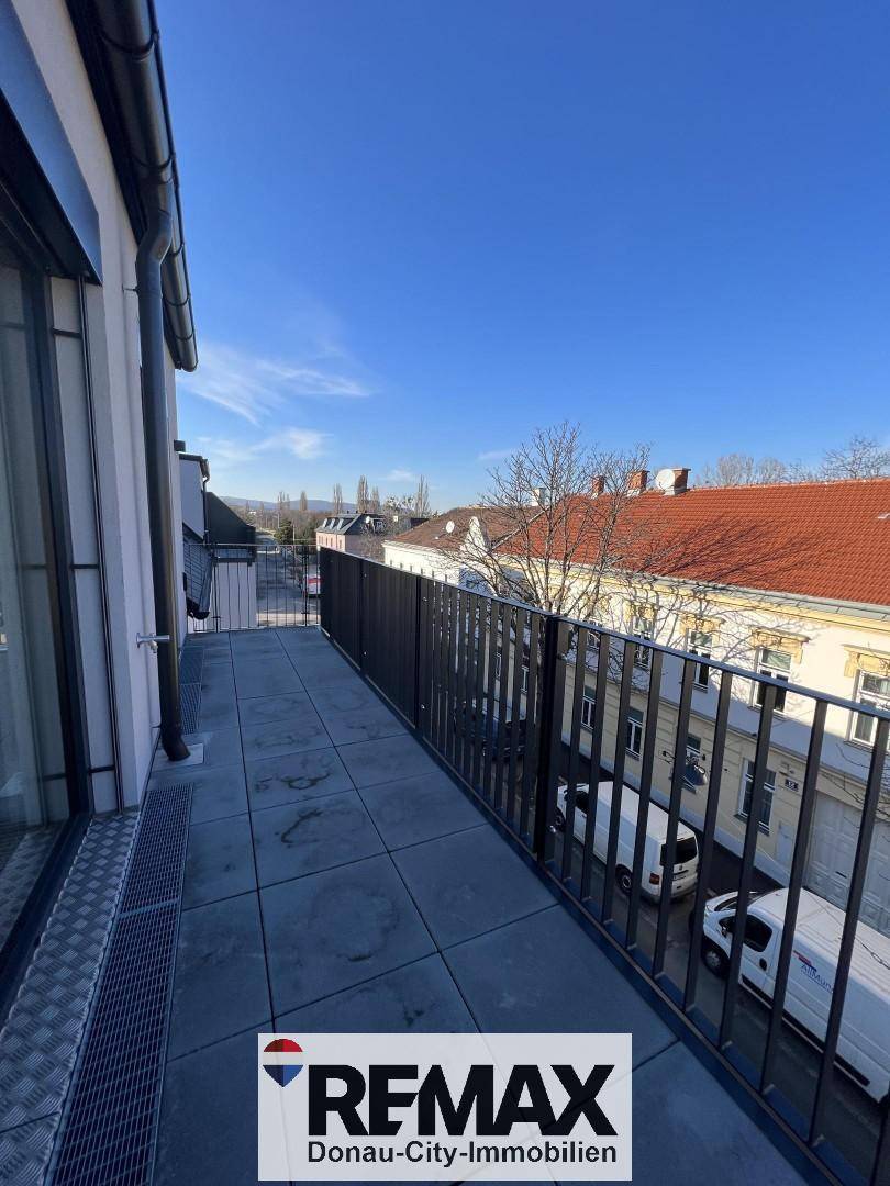 Langer, schmaler Balkon mit Fliesenboden und Blick auf die umliegenden Gebäude.
