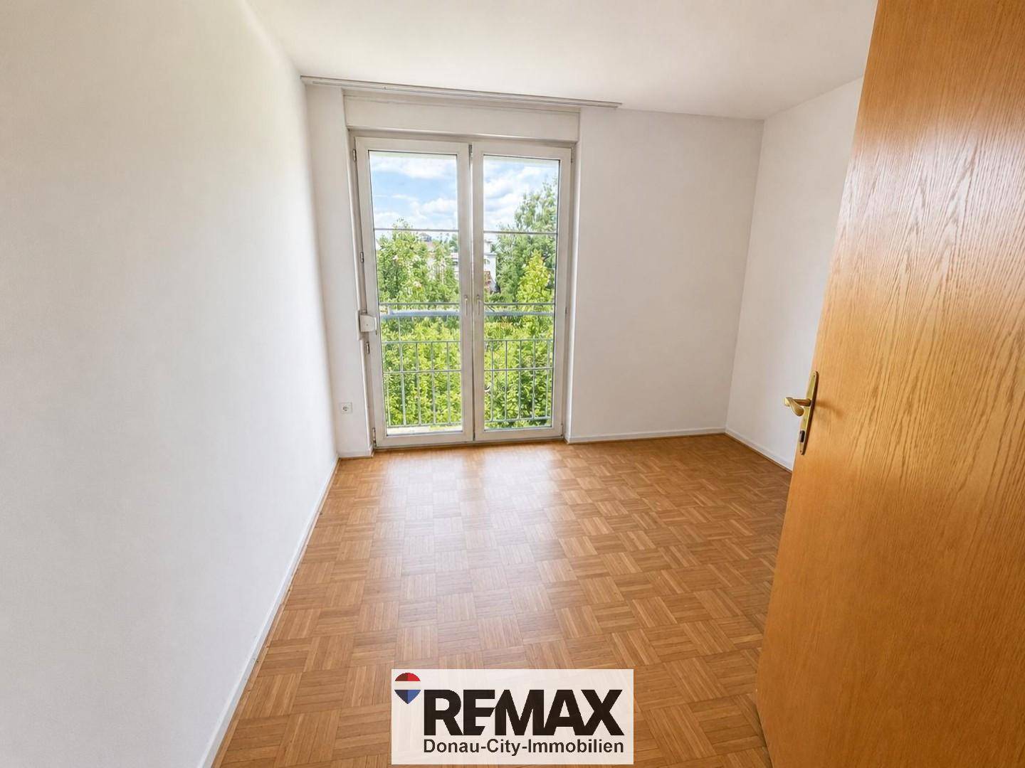 Helles Schlafzimmer mit Parkettboden und Zugang zu einem französischen Balkon mit Blick ins Grüne.