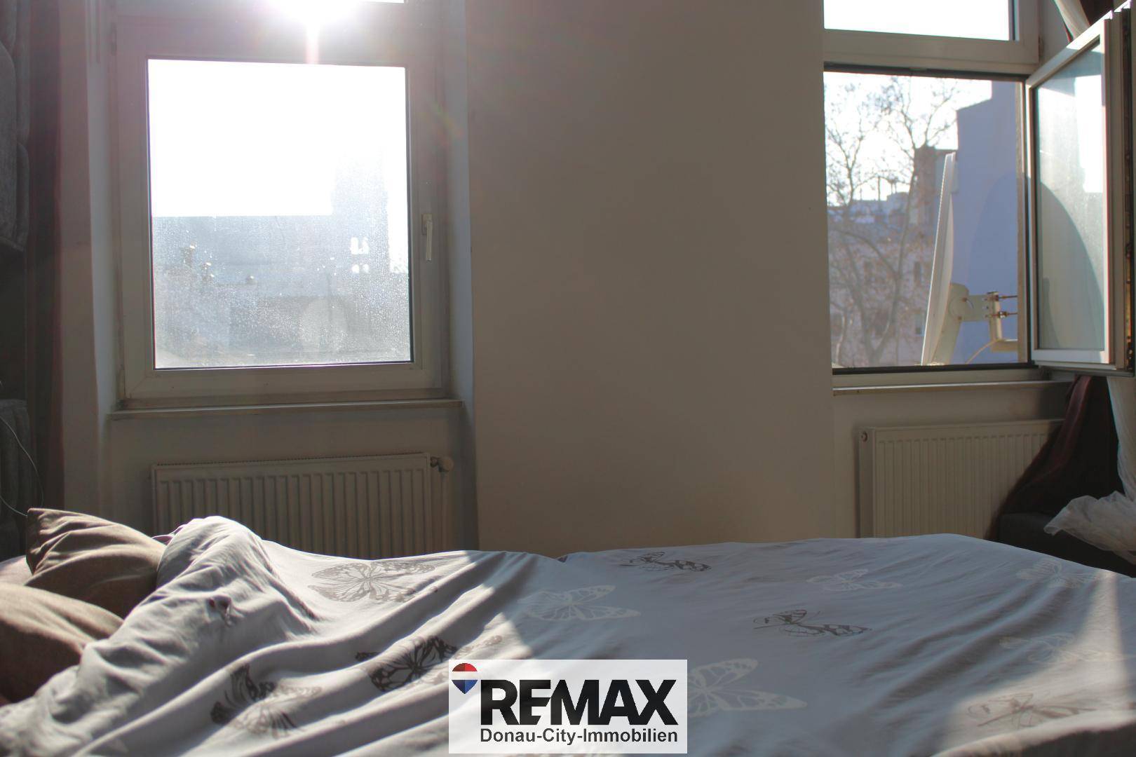 Helles Schlafzimmer mit großem Bett, Heizkörpern unter den Fenstern und viel Sonnenlicht.