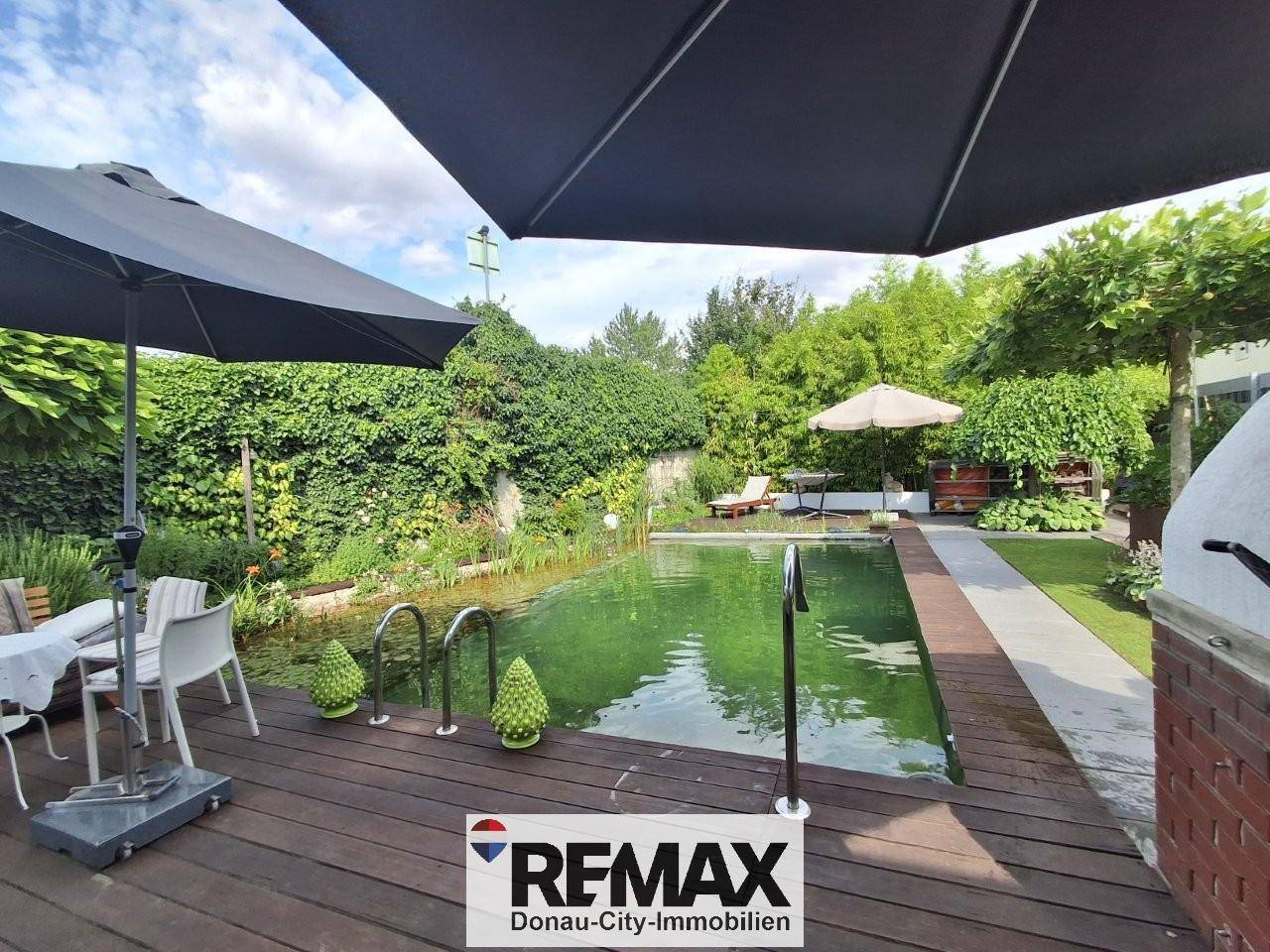 Entspannender Poolbereich im Garten mit Holzdeck, Sonnenschirmen und Liegestühlen.