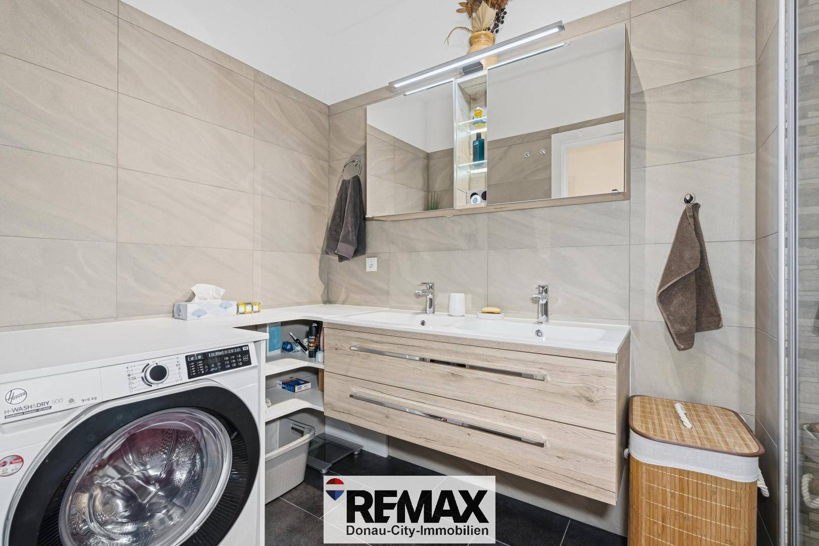 Modernes Badezimmer mit Doppelwaschbecken, Spiegelschrank und integrierter Waschmaschine.
