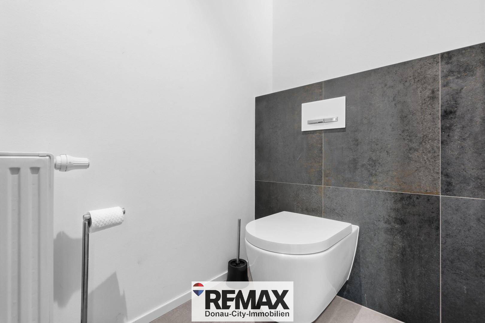 Modernes WC mit Wand-Toilette und dunklen Fliesen an der Wand.