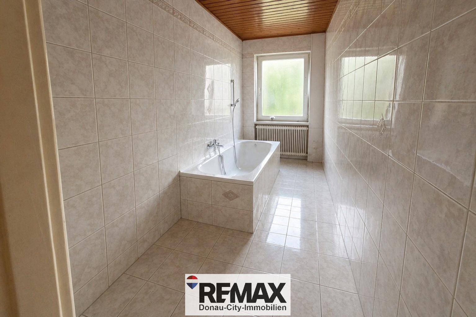 Helles Badezimmer mit Badewanne, Fliesen und Holzdecke.