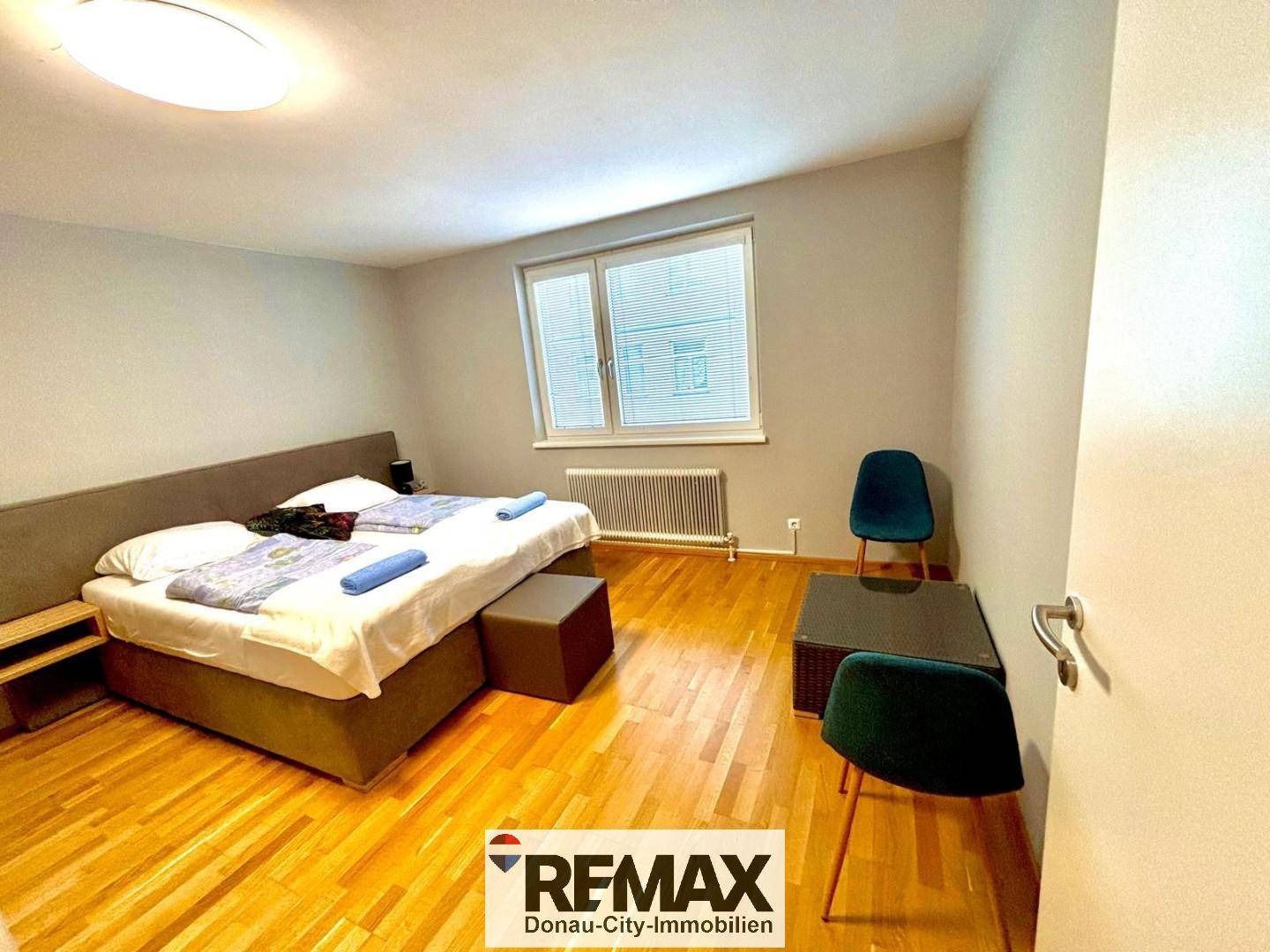 Helles Schlafzimmer mit Doppelbett, Holzboden und großem Fenster.