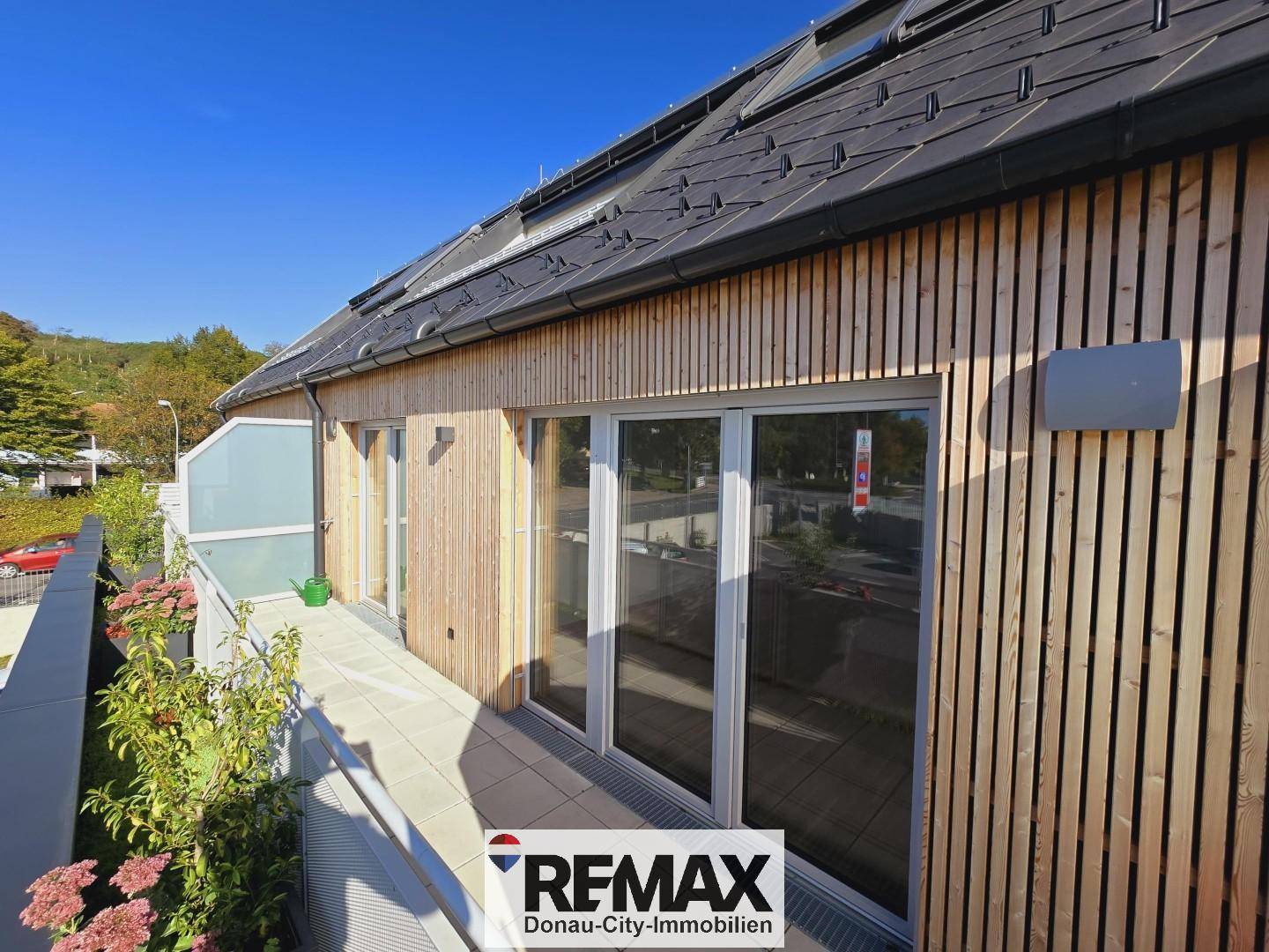 Moderne Gebäudefassade mit Holzverkleidung, großen Fenstern und einem sonnigen Balkon.