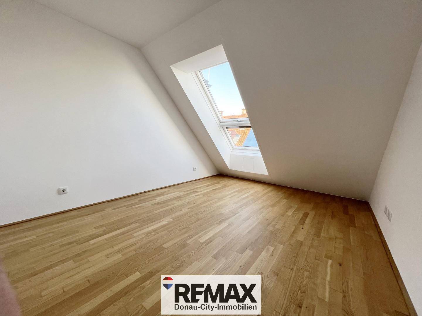 Leeres Schlafzimmer mit Holzboden und Dachfenster, bietet viel natürliches Licht und Raum.