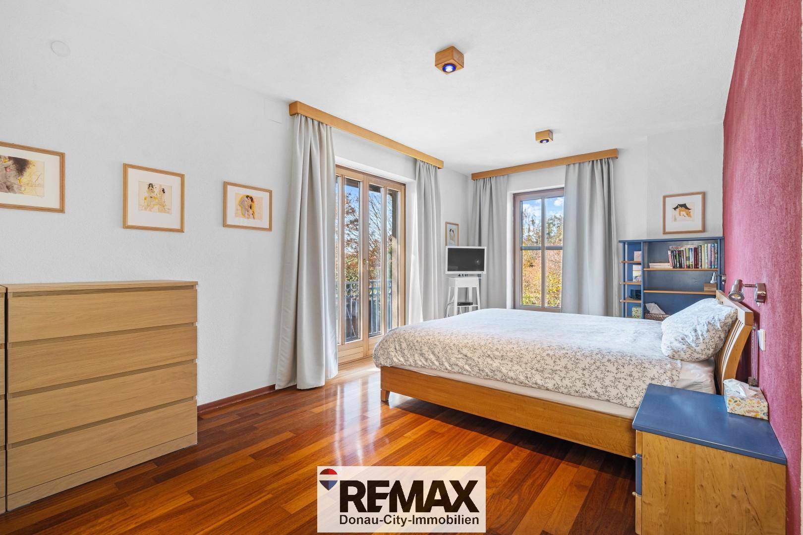 Schlafzimmer mit Holzboden, Zugang zum Balkon und Blick ins Grüne.