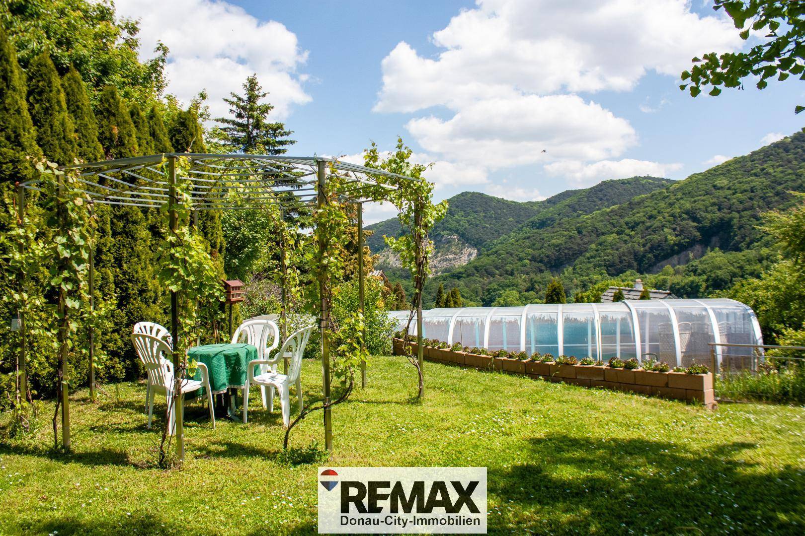 Idyllischer Gartenbereich mit Sitzgelegenheit unter einer Pergola und Blick auf die umliegende Natur.