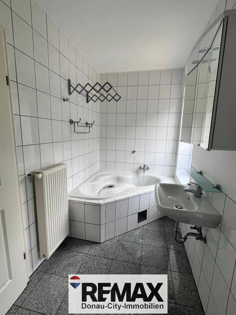 Badezimmer mit Eckbadewanne, Waschbecken und weißen Wandfliesen.