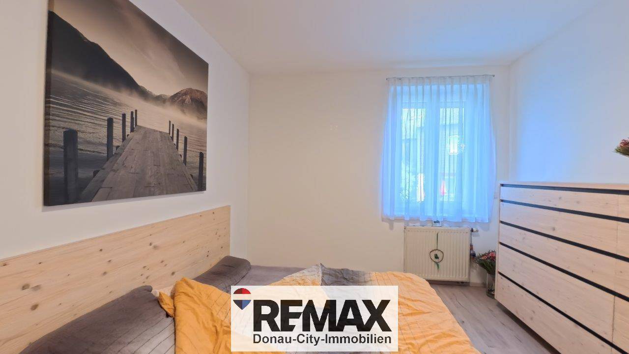 Helles Schlafzimmer mit Holzbett, Kommode und großem Wandbild.