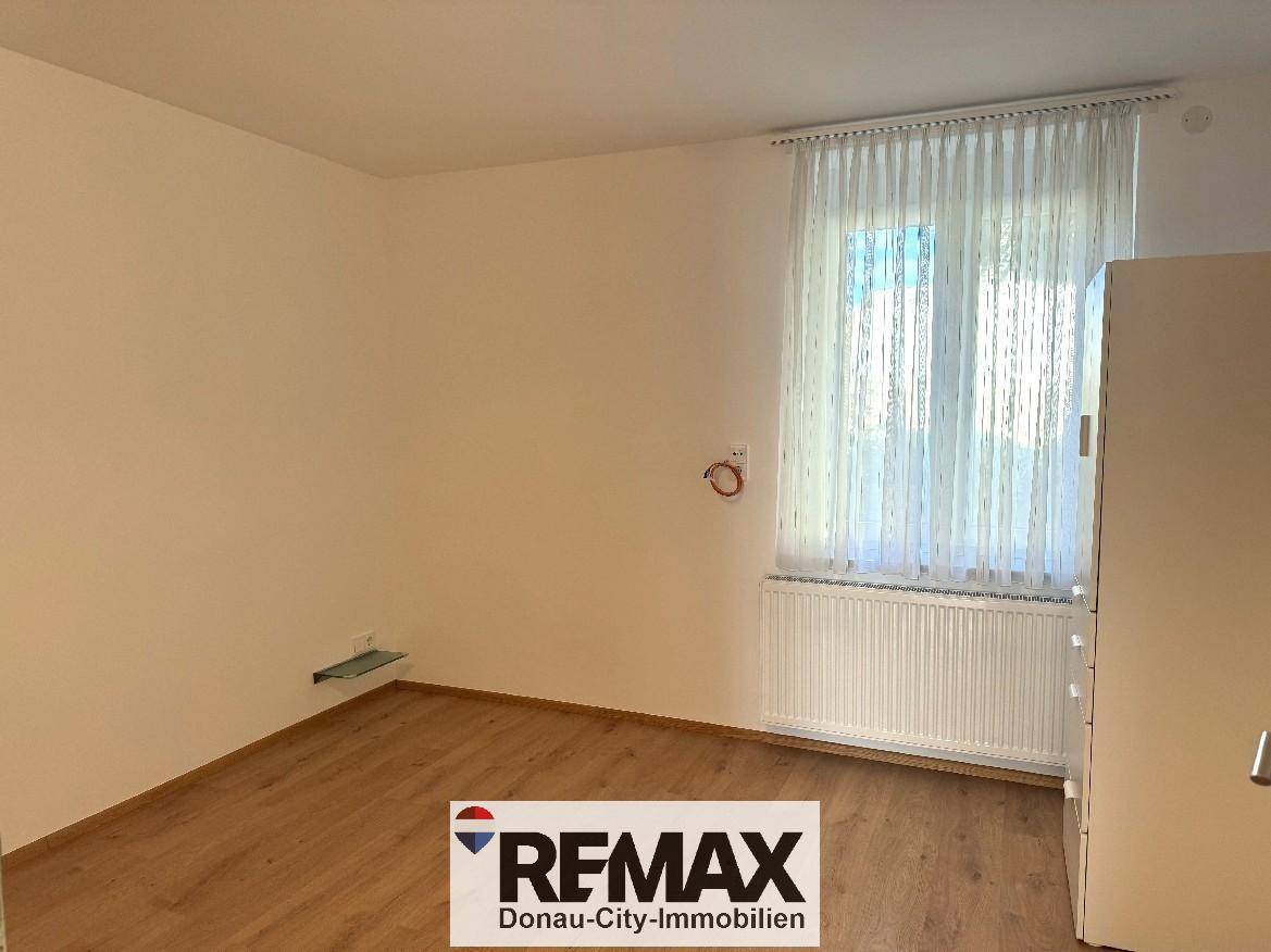 Helles Zimmer mit Laminatboden, weiß gestrichenen Wänden und Fenster mit Heizkörper.