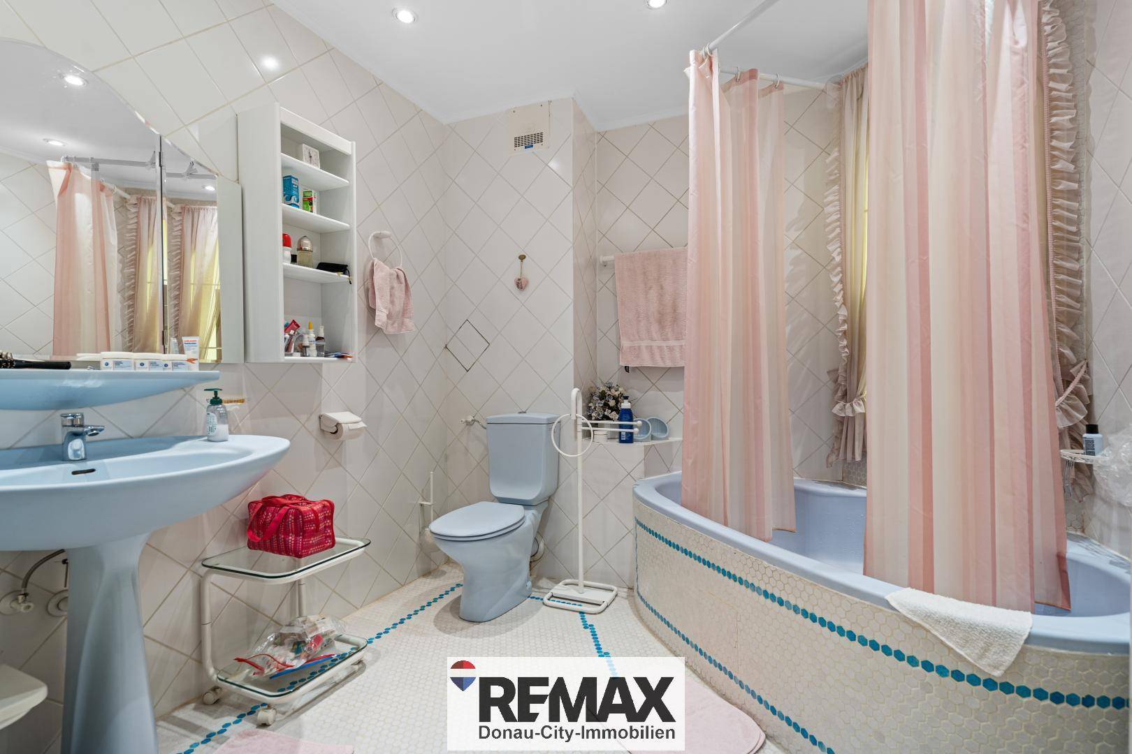 Badezimmer mit Badewanne, Toilette, Waschbecken und hellen Fliesen, im Stil der 80er Jahre.