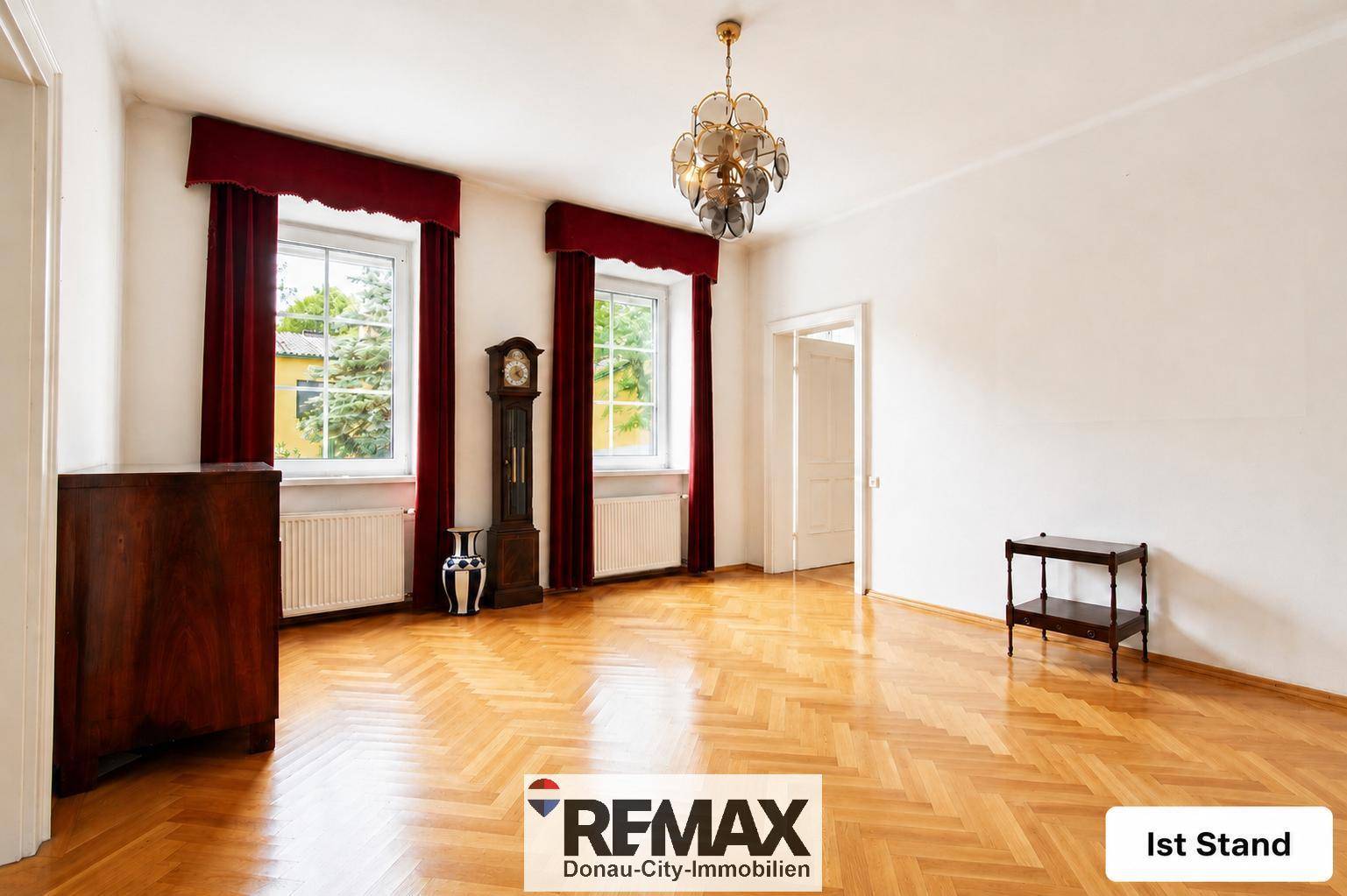 Geräumiges Wohnzimmer mit Parkettboden und großen Fenstern, unmöbliert und hell.
