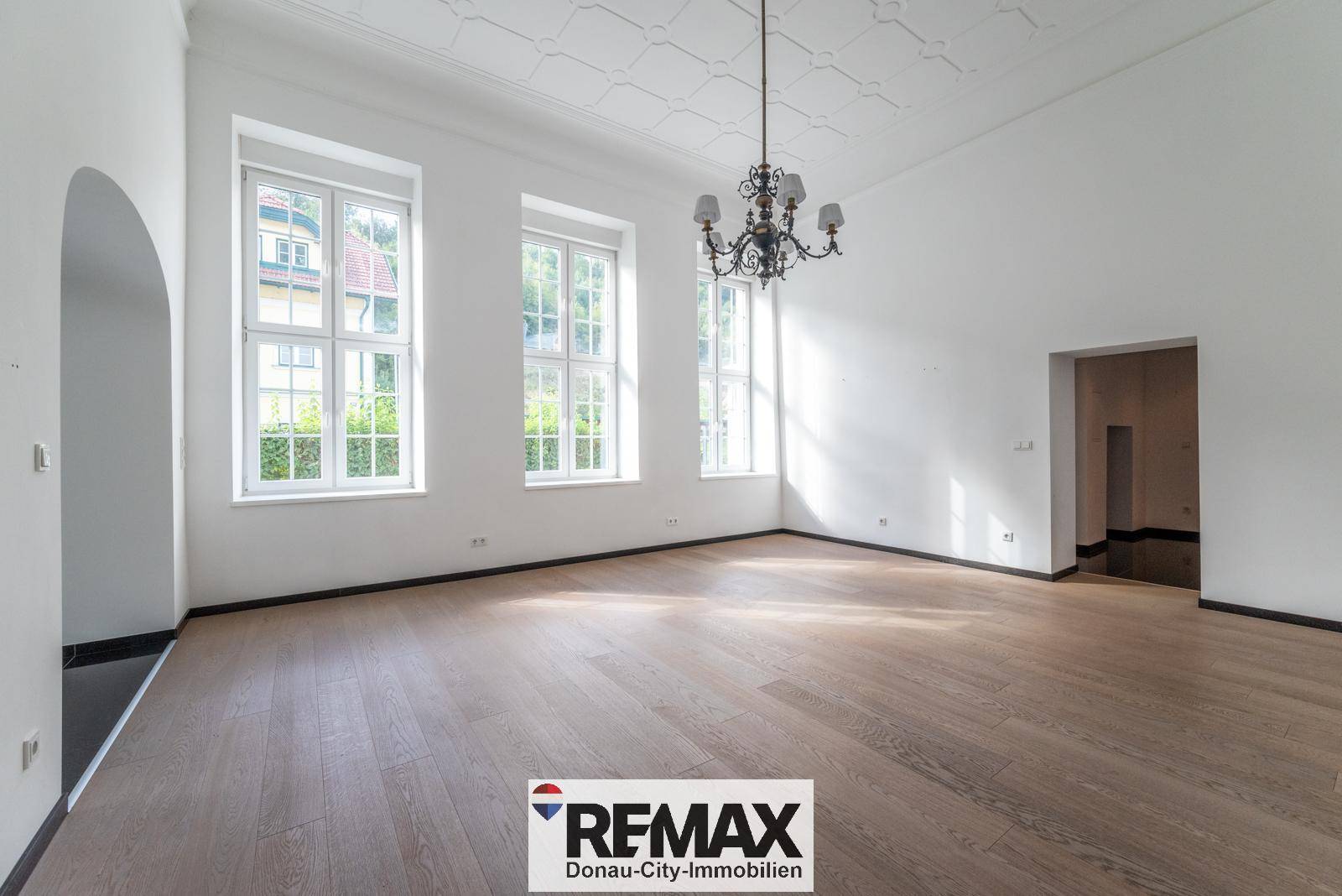Geräumiges Wohnzimmer mit elegantem Parkettboden, hohen Decken und einem Kronleuchter.