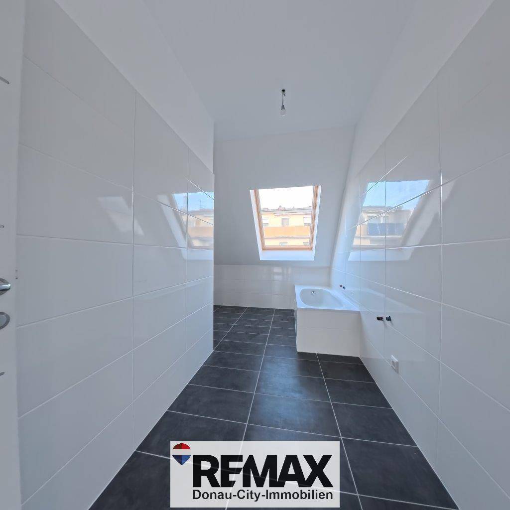 Modern gefliestes Badezimmer im Dachgeschoss mit Badewanne, Dachfenster und schrägen Wänden.