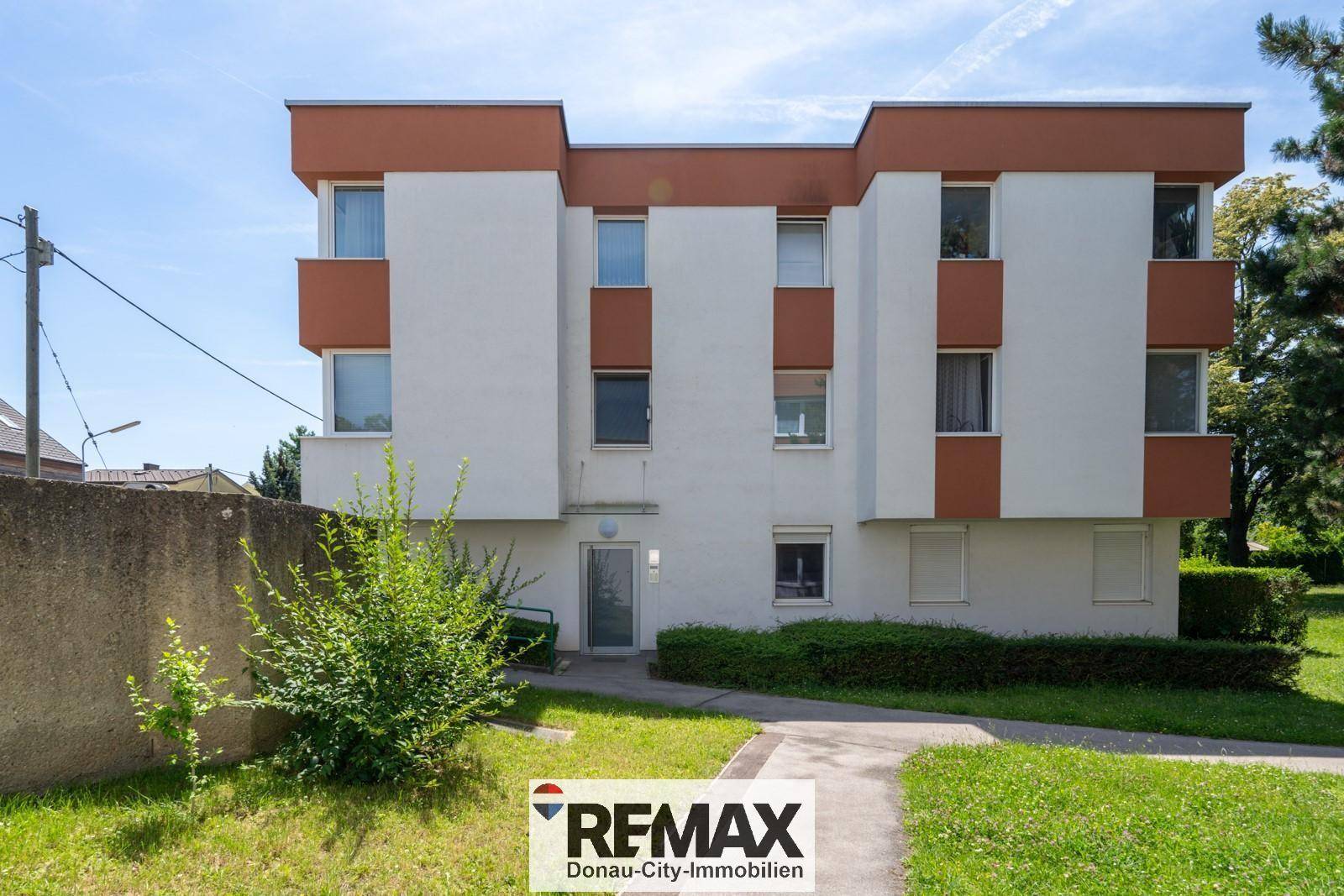 Modernes Wohngebäude mit weißer Fassade, braunen Akzenten und Grünflächen.