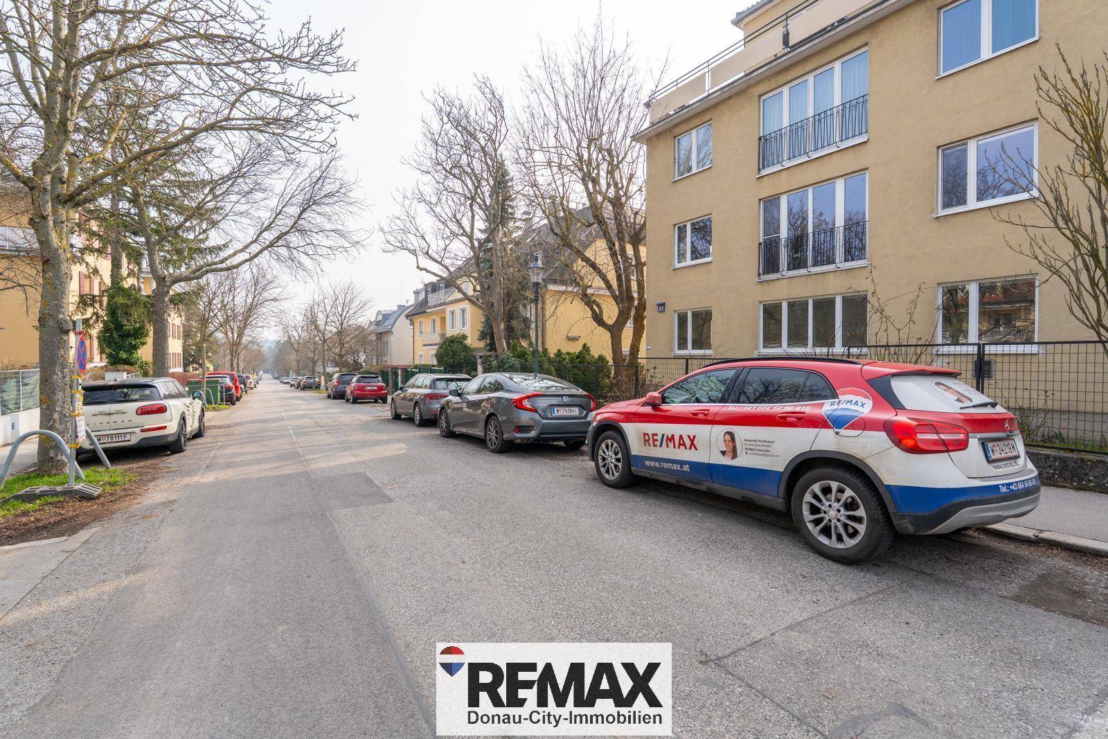 Ruhige Wohnstraße mit geparkten Autos und einem Mehrfamilienhaus im Hintergrund.
