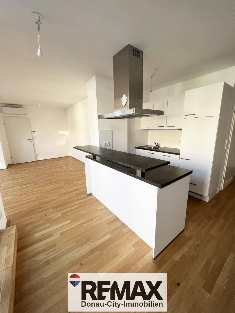 Moderne, offene Küche mit weißer Küchenzeile, Kochinsel und hellem Holzparkettboden.
