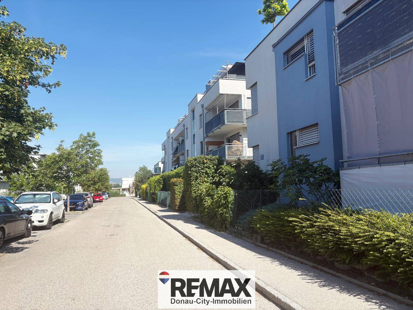 Reihe moderner Wohngebäude entlang einer Straße mit Balkonen und gepflegten Hecken.