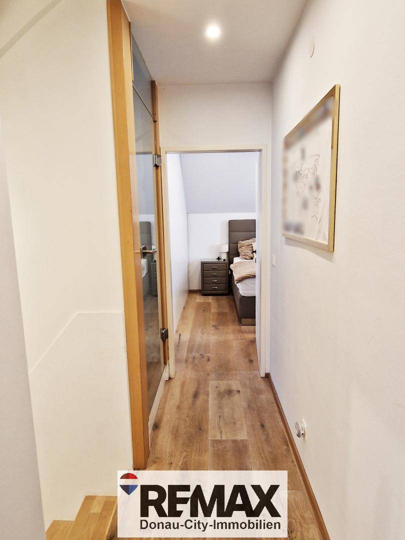 Flur mit Holzfußboden und moderner Glastür, die zu einem Schlafzimmer führt.