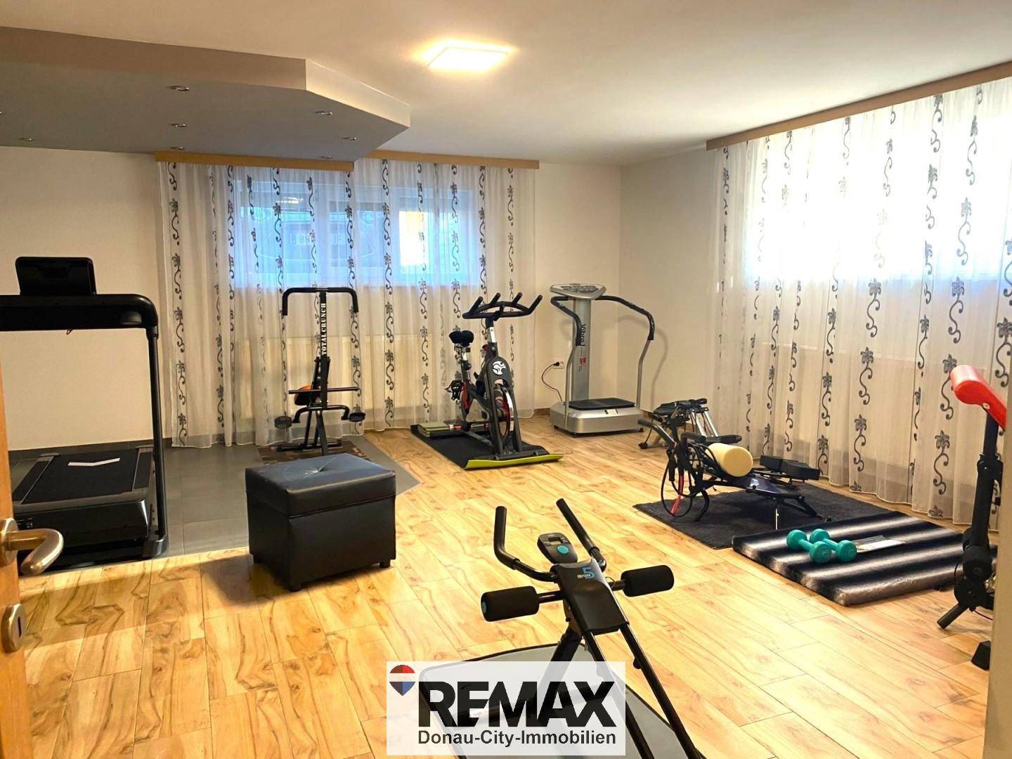 Geräumiger Fitnessraum mit verschiedenen Trainingsgeräten und Holzfußboden.