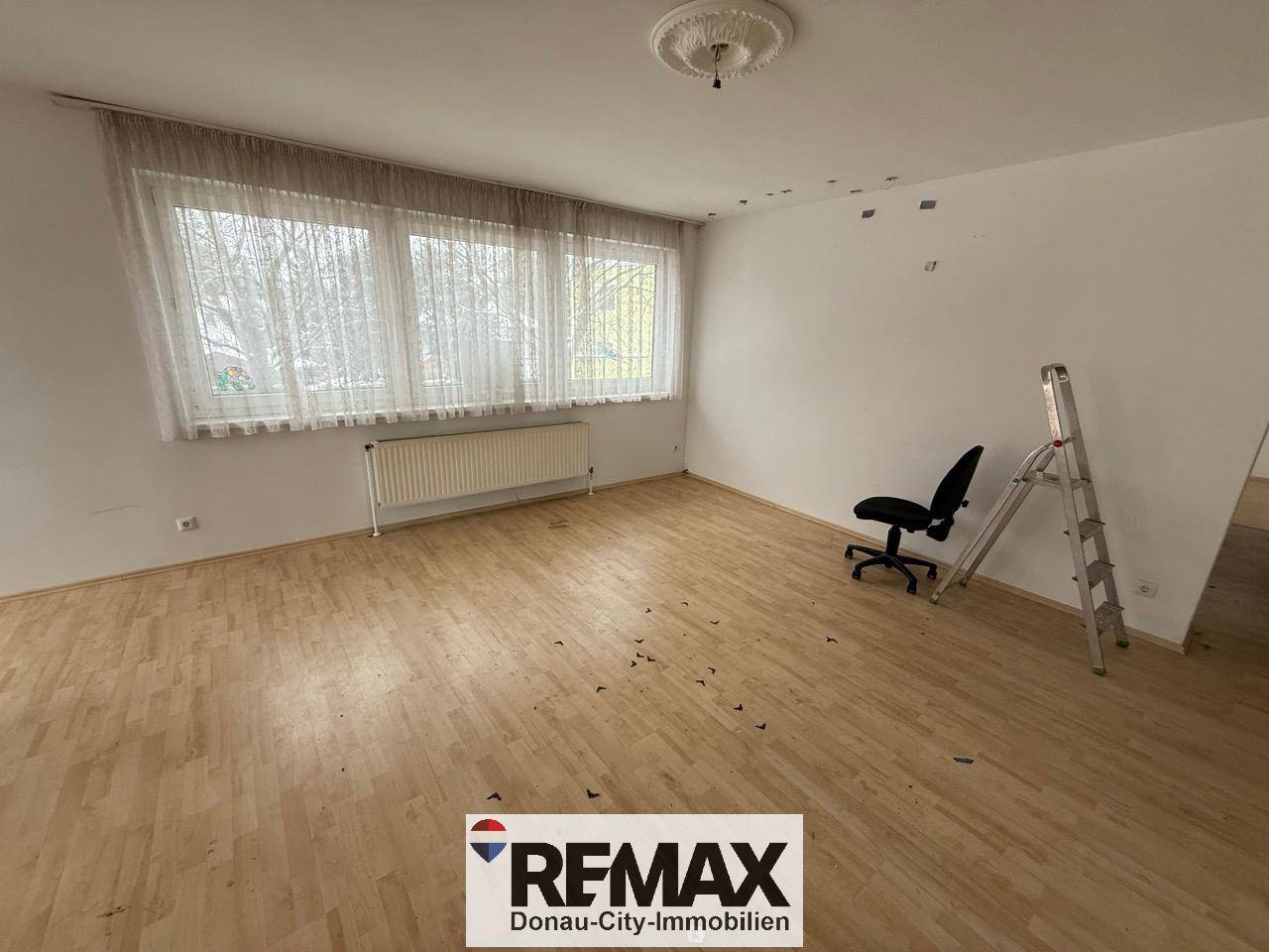 Geräumiges Wohnzimmer mit Laminatboden und großen Fenstern, die für eine helle Atmosphäre sorgen.