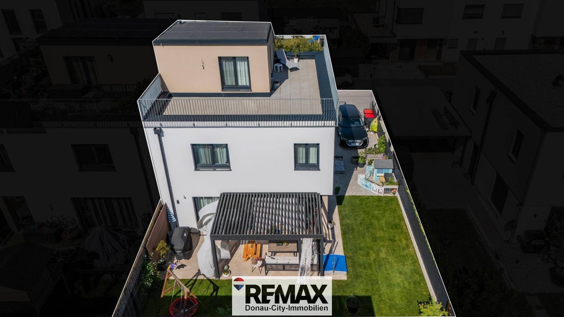 Vogelperspektive eines modernen Hauses mit Garten, Terrasse und Dachterrasse in städtischer Umgebung.
