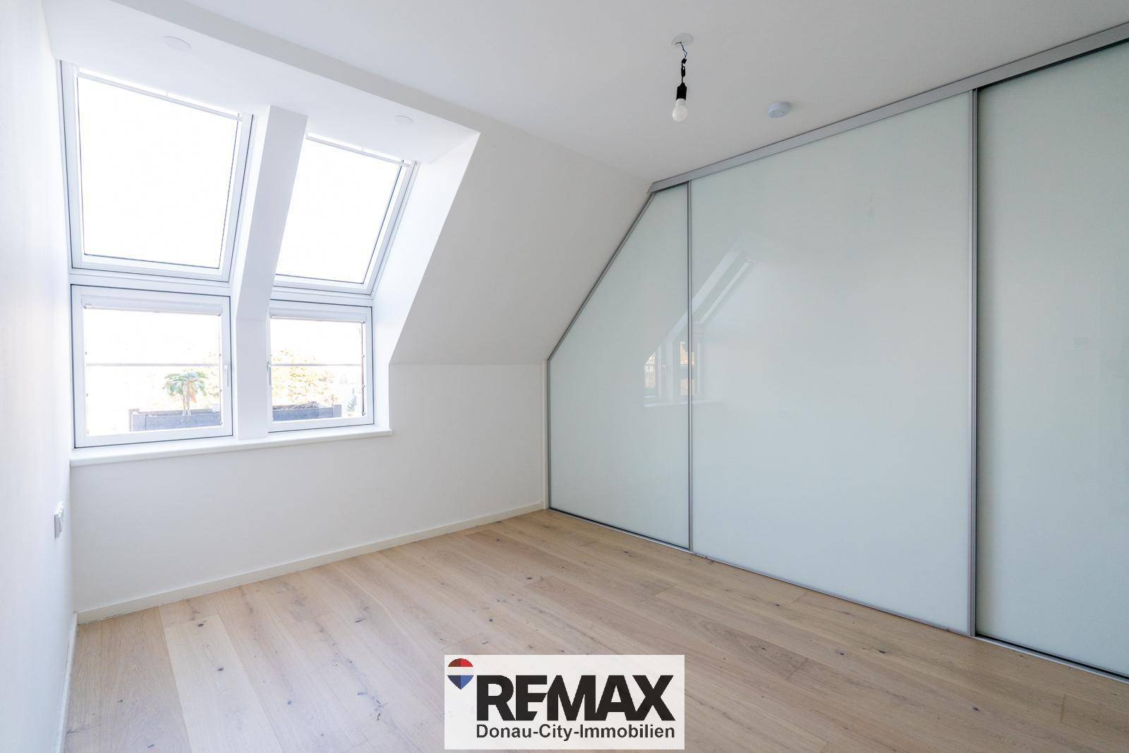 Geräumiges Schlafzimmer mit viel Tageslicht durch Dachfenster und praktischem Einbauschrank.