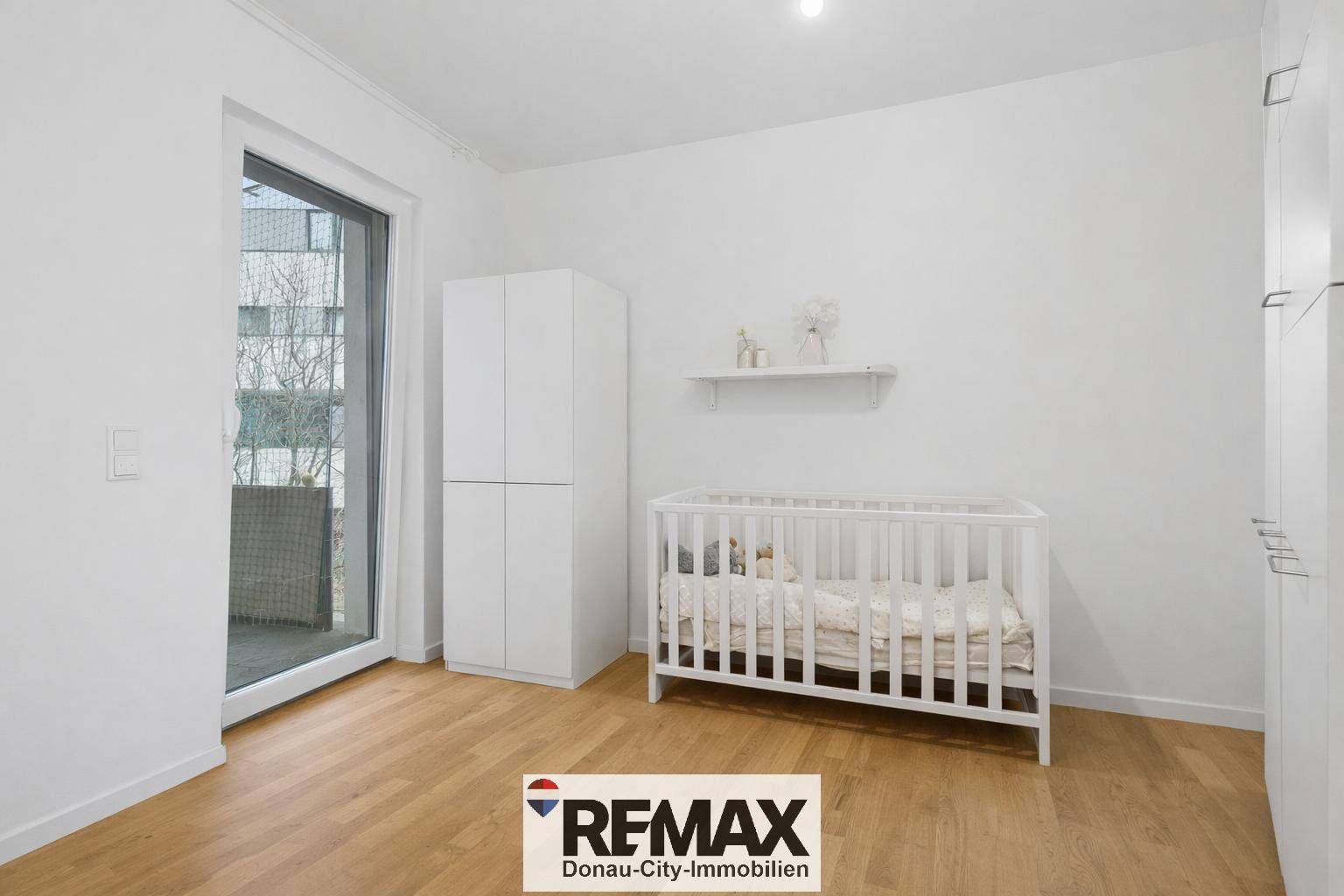 Kinderzimmer mit Babybett, weißem Schrank und Zugang zu einem Balkon.