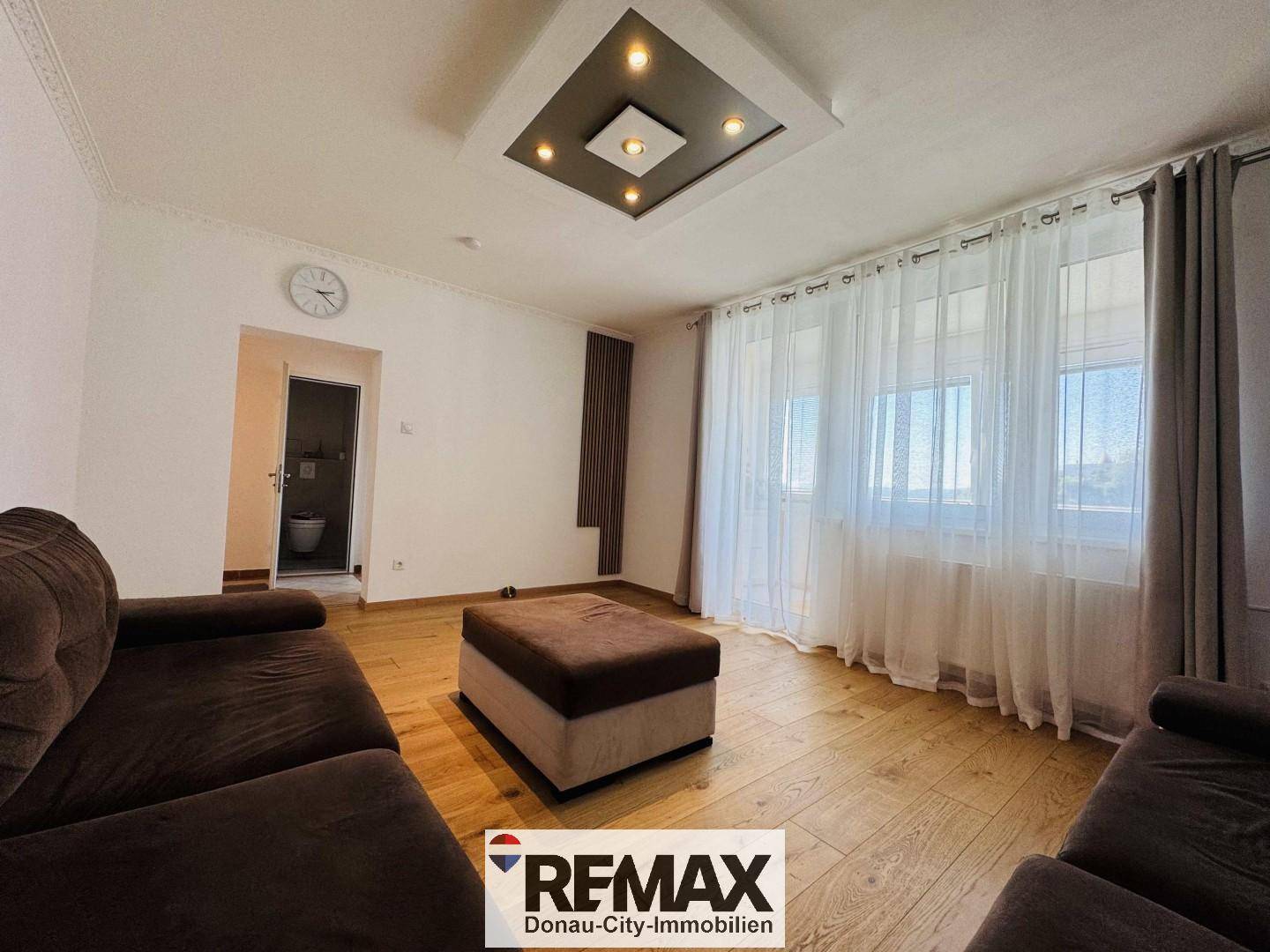 Helles Wohnzimmer mit Parkettboden, braunen Sofas und Blick auf ein separates WC.